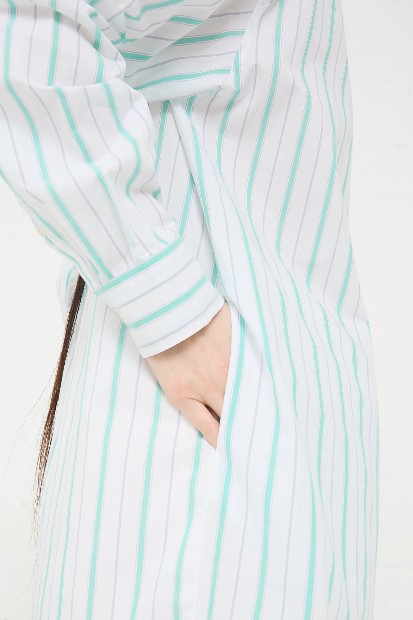 Close-up of a person with their hand in the pocket of a Baserange Organic Cotton Ole Shirt Dress in Stripe.