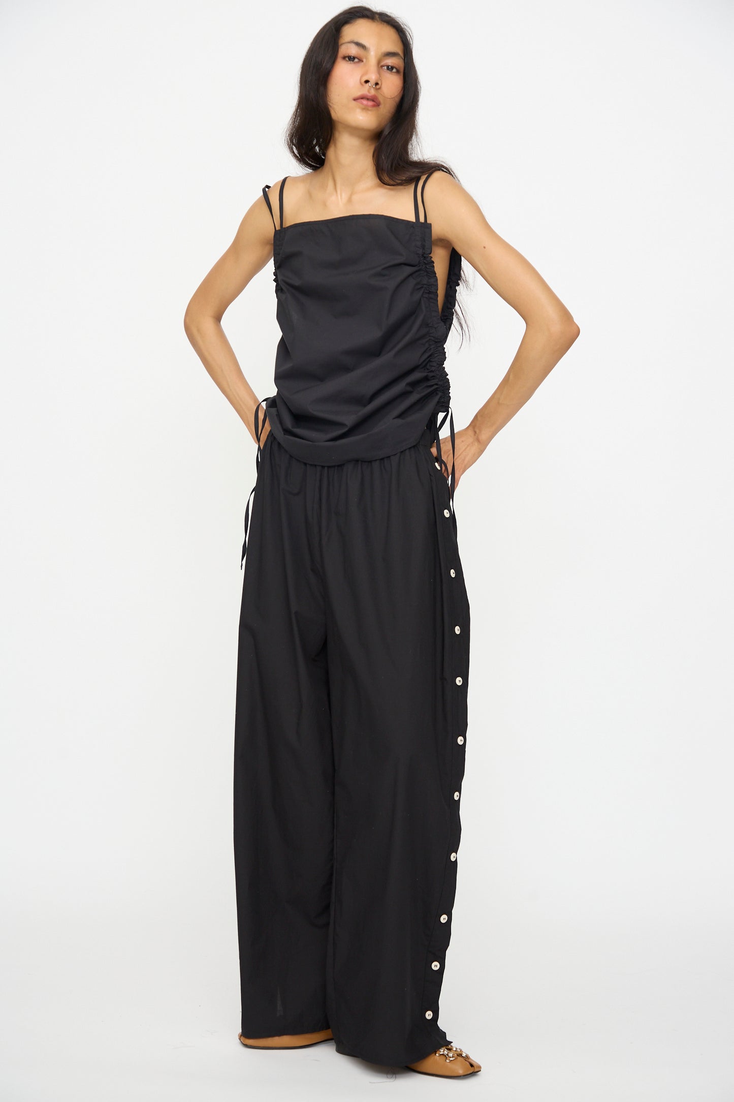 A woman models Baserange’s Part Pants in Black—loose cotton poplin wide-leg pants with an elastic waist—paired with a sleeveless black top, standing against a plain white background.
