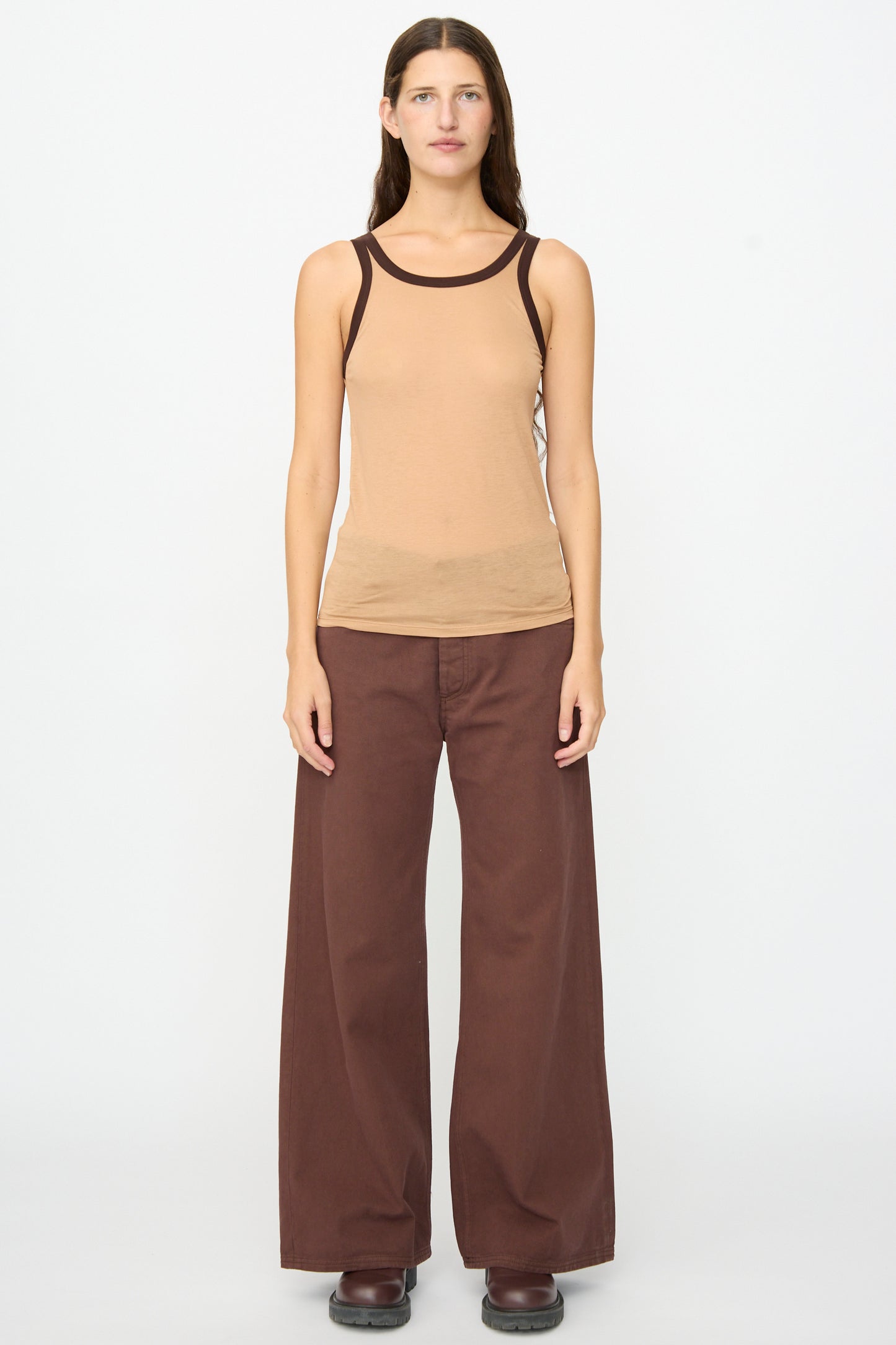 A person stands facing forward against a plain white background, wearing the Baserange Racer Tank in Aural Tactile, paired with wide brown pants and dark shoes.
