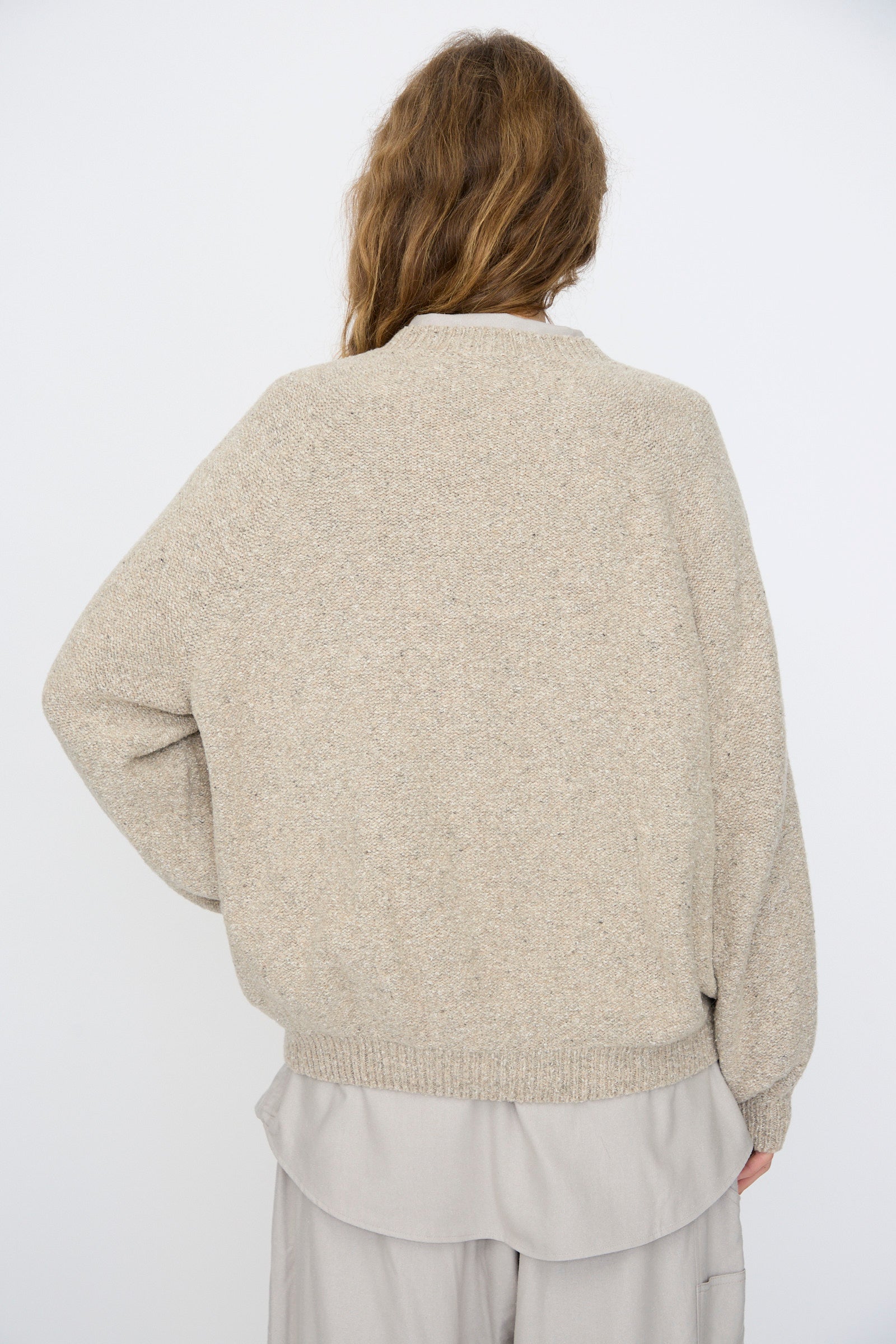 Person with long brown hair wears the Baserange Recycled Wool Soar Sweater in Ingra Sand, photographed from the back against a plain white background.