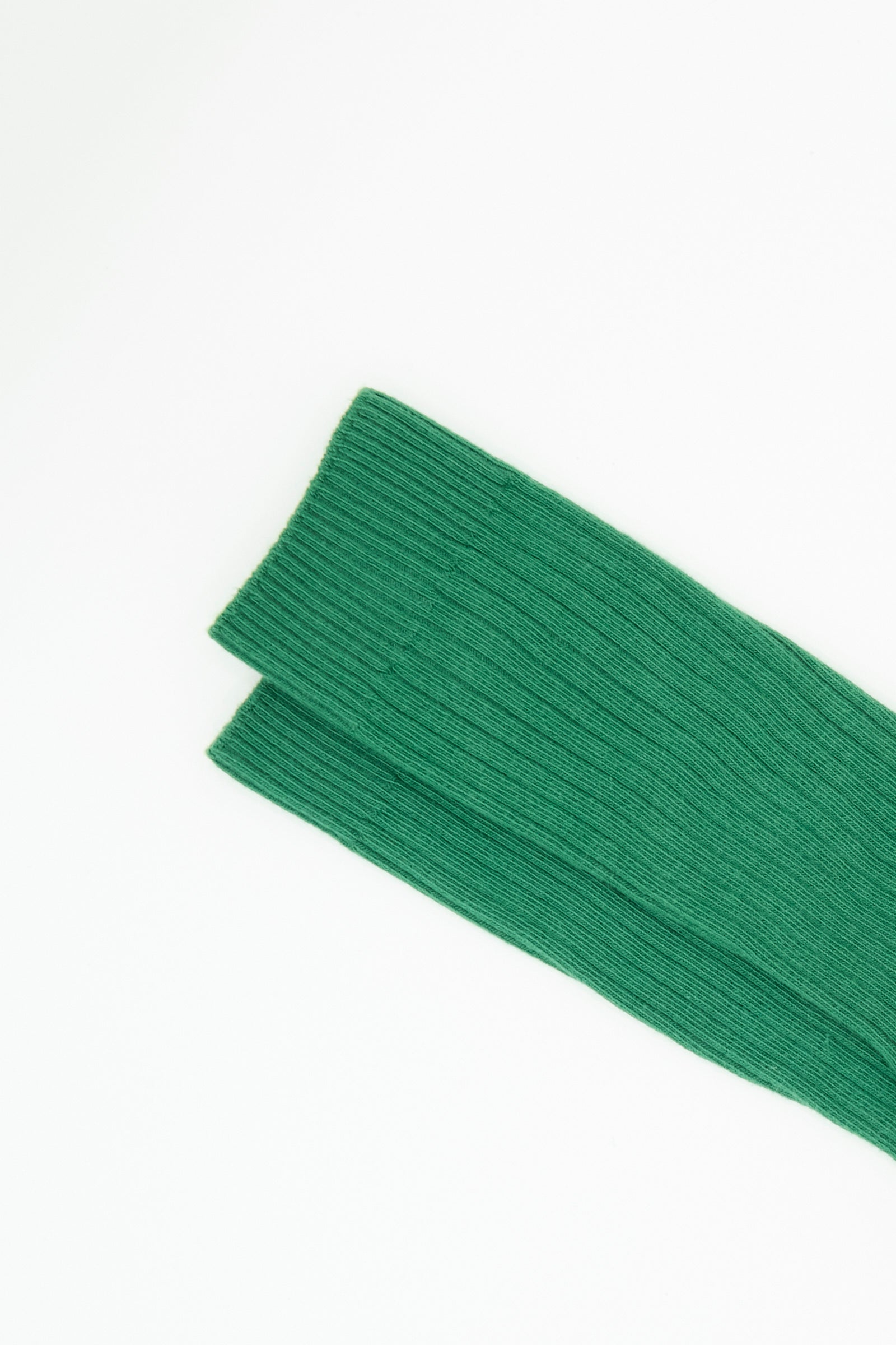 Two pieces of Baserange’s Rib Overankle Socks in Calla Green are positioned diagonally on a white background.