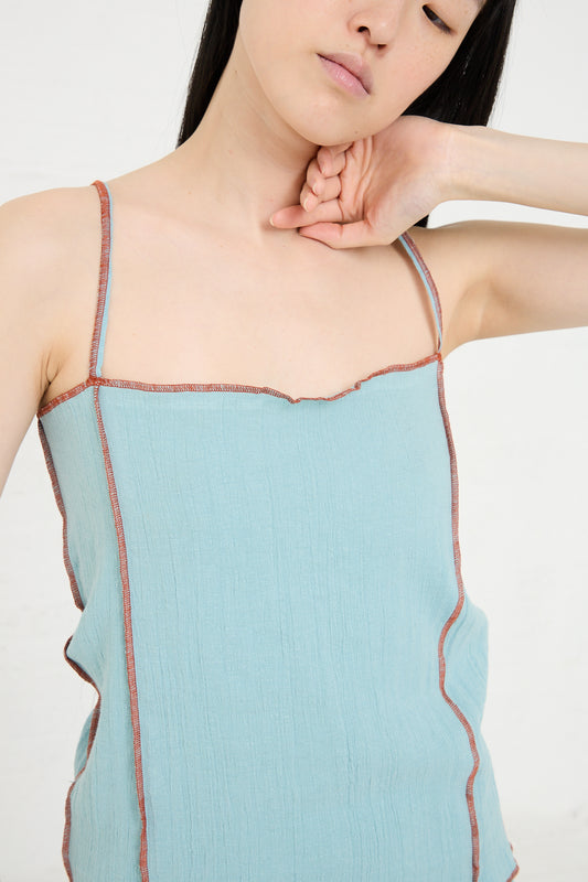 Woman in a Shok Slip Top in Wuxi Blue by Baserange with contrasting trim posing with her hand on her neck.