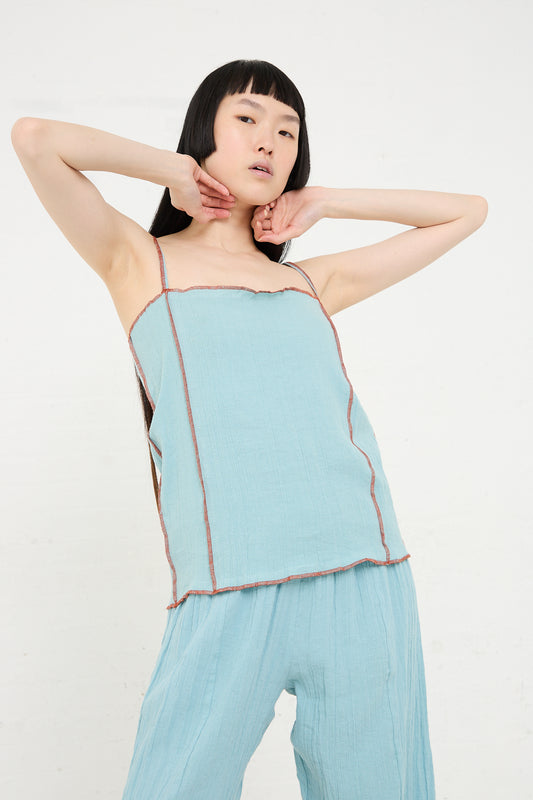 A person posing in a Baserange Shok Slip Top in Wuxi Blue outfit with hands behind their head, standing against a white background.
