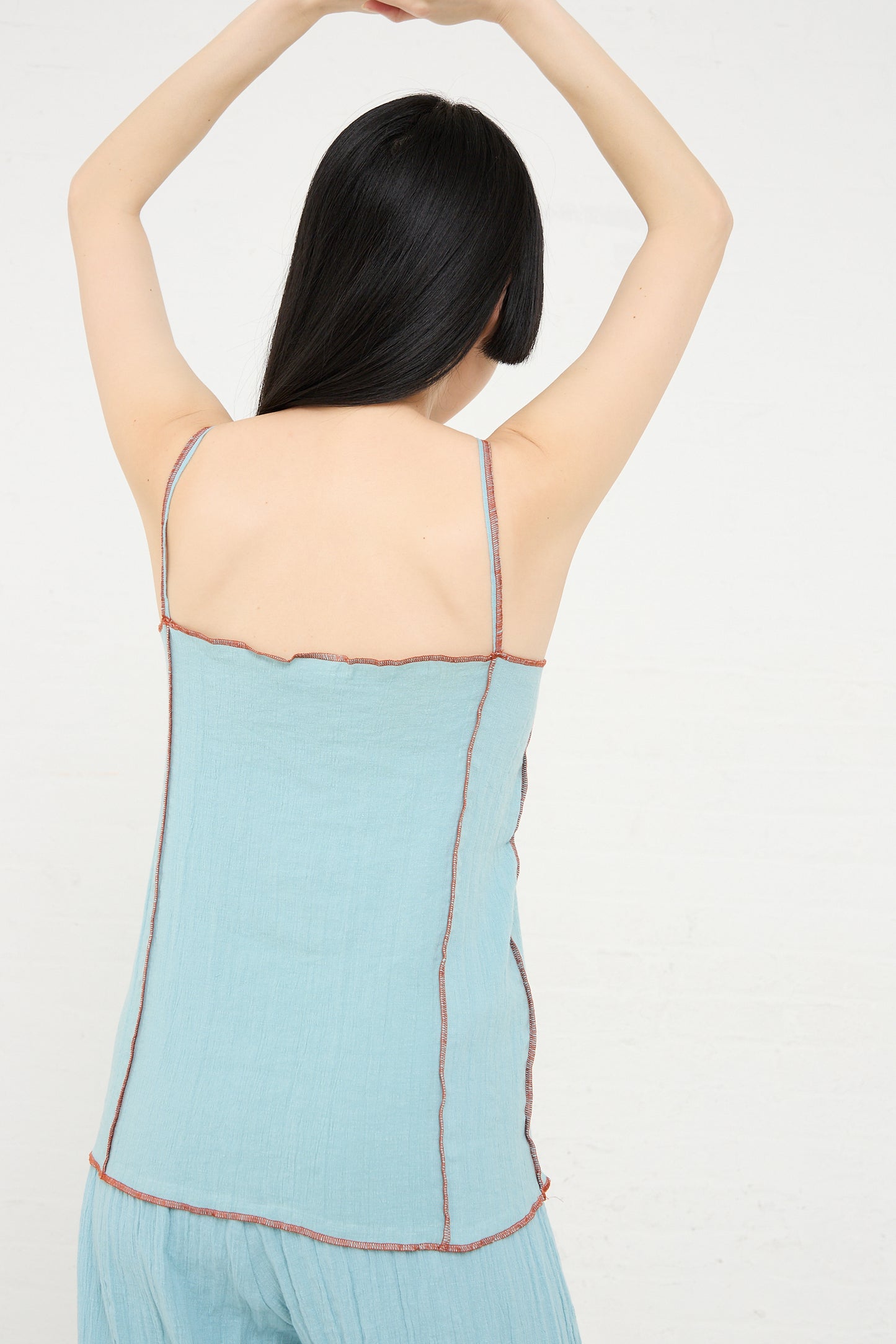 Woman seen from the back wearing a Baserange Shok Slip Top in Wuxi Blue with raised arms.