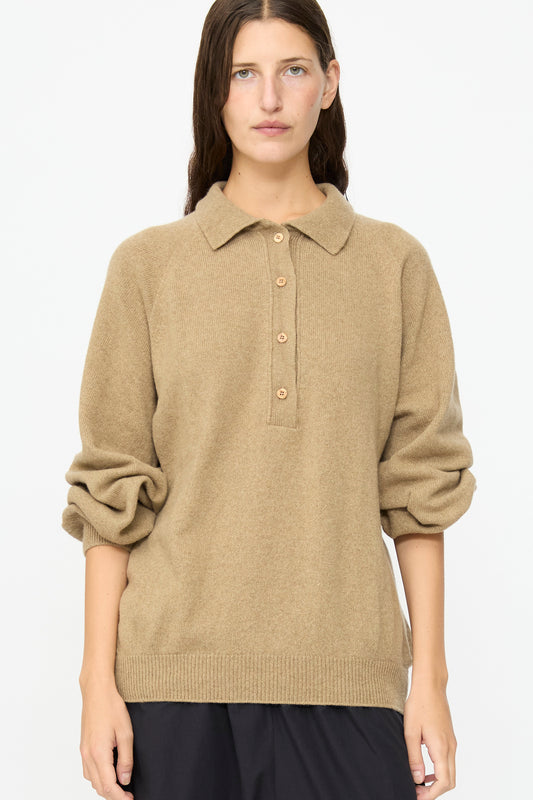 A person wearing the Baserange Soar Polo in Rovere Brown, a beige cotton knit long-sleeve sweater with a collar and buttons, stands against a plain white background.