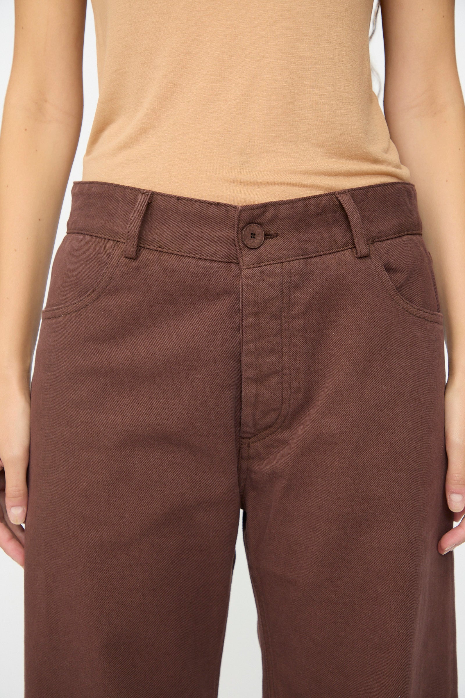 Model wearing the Baserange Tajo Pant Wide in Cata Brown with a beige shirt, shown from mid-torso to upper thighs, hands relaxed at sides.
