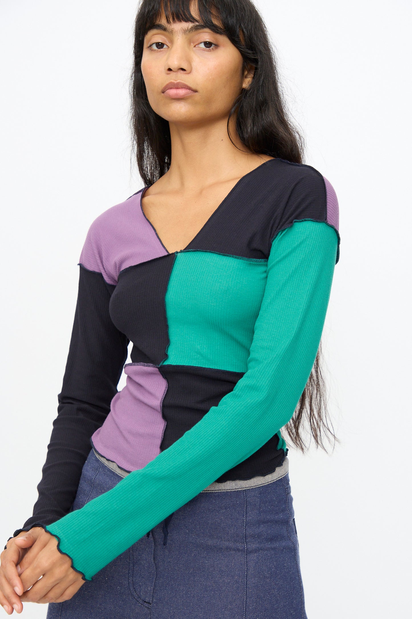A woman models the Baserange Teak Long Sleeve Tee in green, navy, and purple against a plain background, highlighting this stylish color-block shirt.