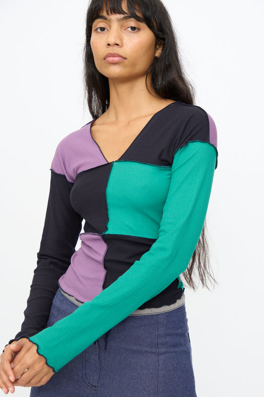 A woman models the Baserange Teak Long Sleeve Tee in green, navy, and purple against a plain background, highlighting this stylish color-block shirt.