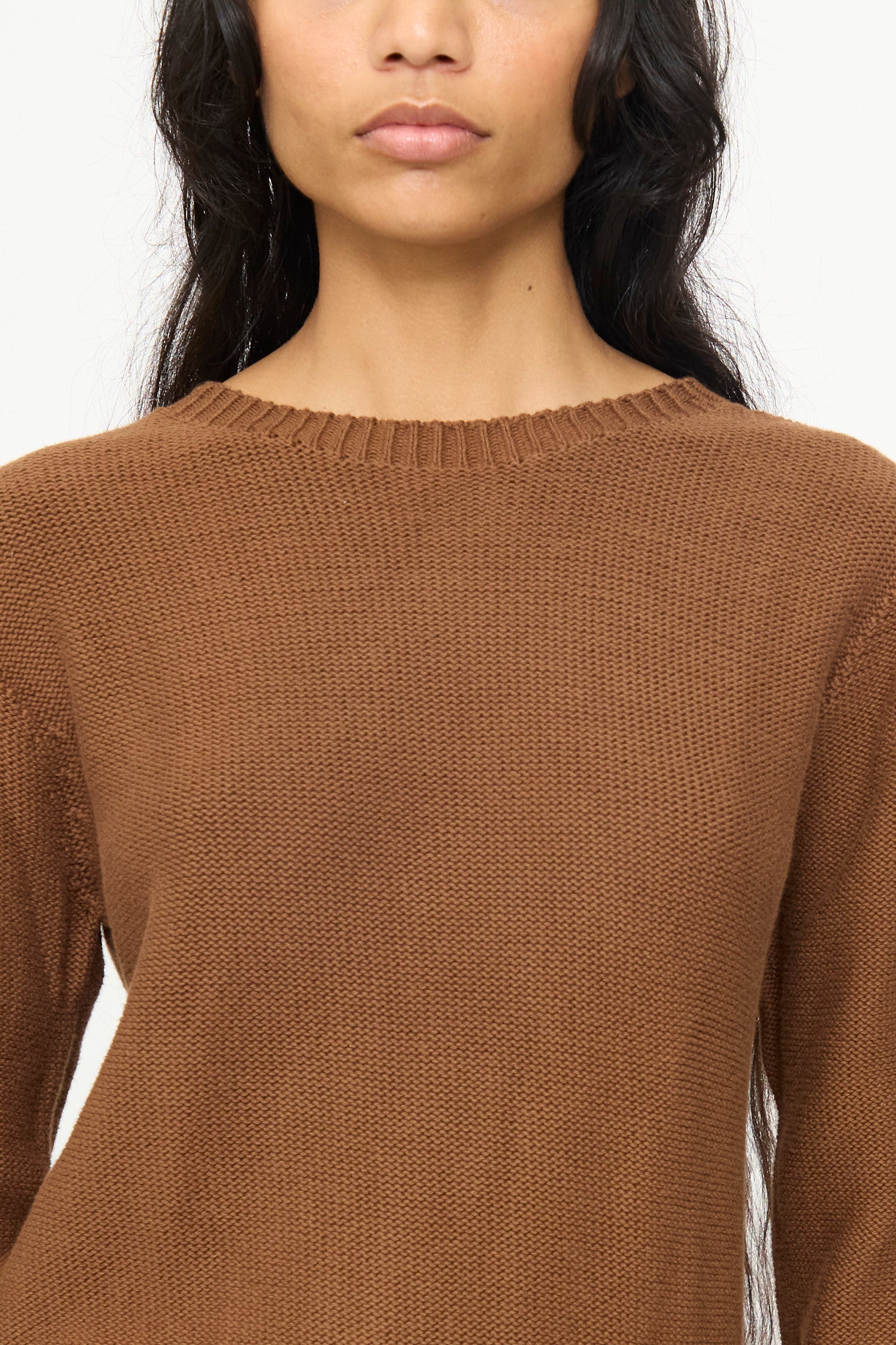 A person with long dark hair and a neutral expression is shown from shoulders to mid-torso wearing the Baserange Tier Sweater in Nocciola Brown.