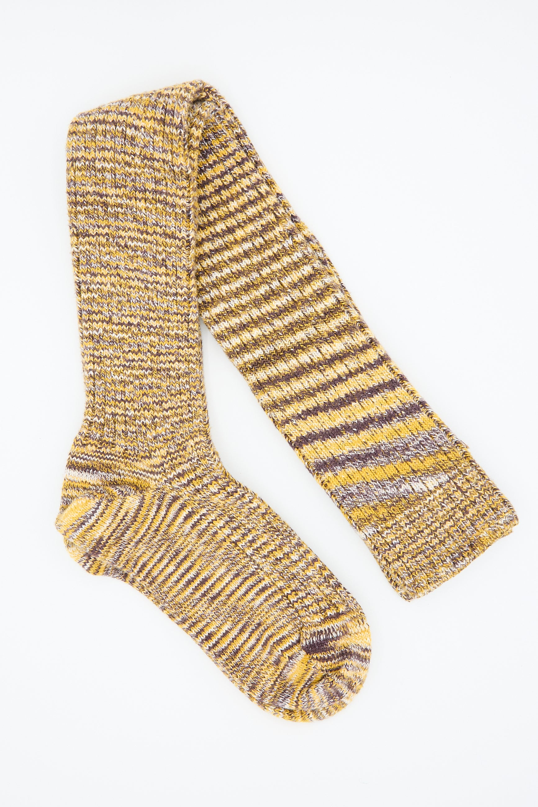 The Baserange Twisted Overknee Sock in Brown Multicolor is crafted from organic cotton yarn and showcases a striking blend of yellow, brown, and purple hues. The sock uniquely combines rib knit patterns with uniform sections for a stylish look.