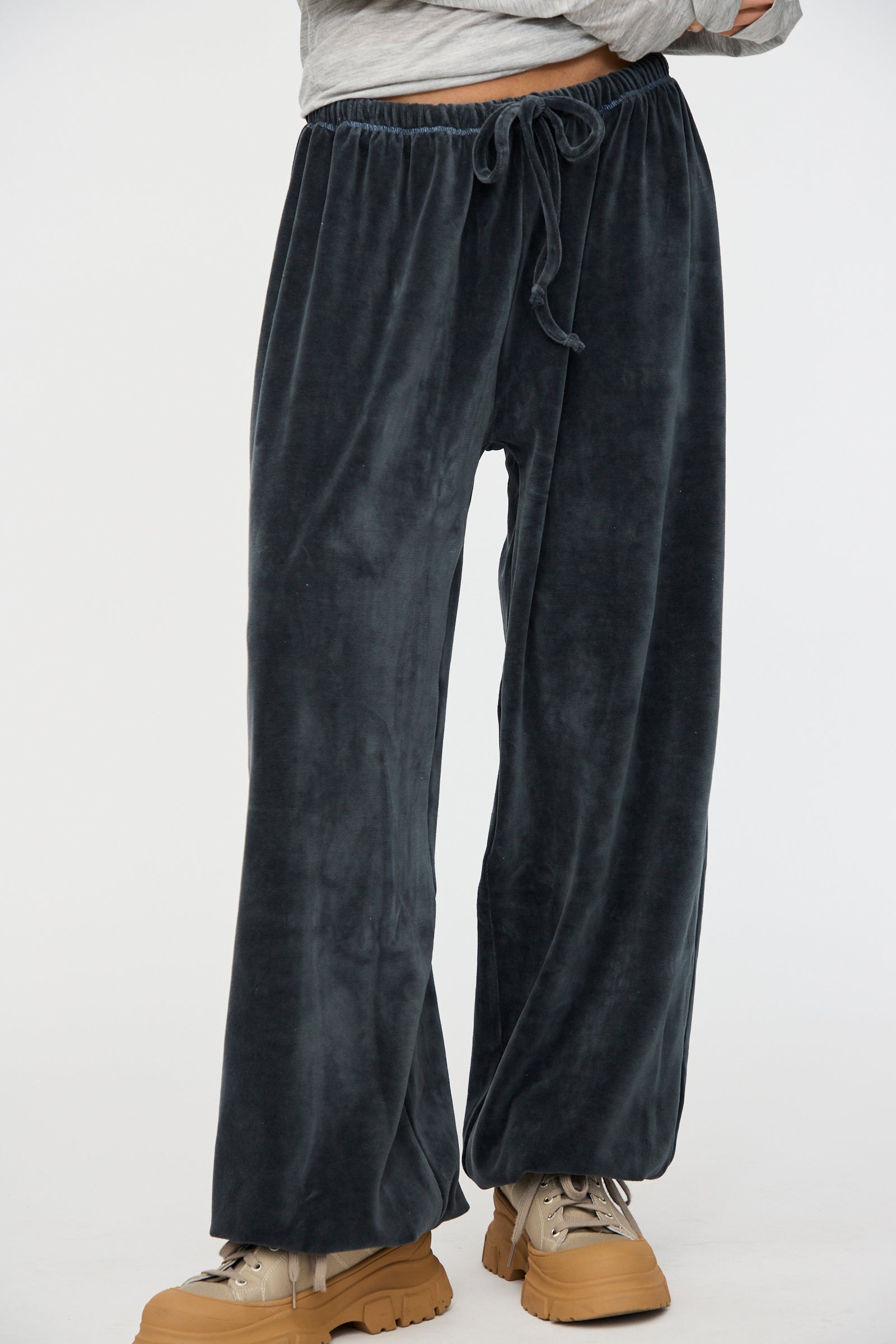 Someone is wearing Baserange Velour Pillow Pant in Petroleum Blue, featuring an elastic waistband and drawstring, paired with tan chunky shoes.