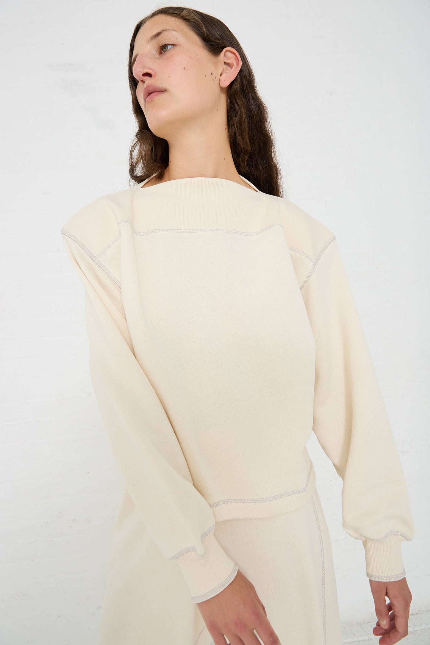 Person wearing a beige, long-sleeved, boatneck Way Boat Sweatshirt in Undyed Path Grey by Baserange stands against a plain white background.