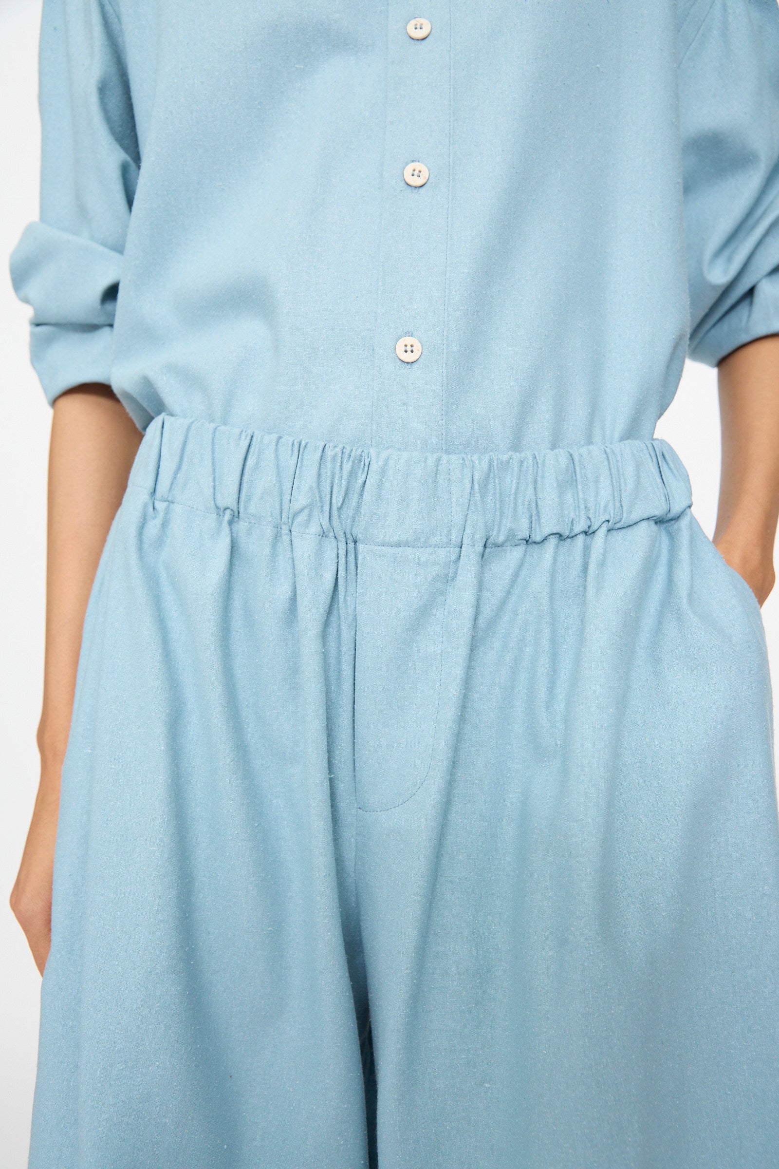 A person wearing Baserange's Wild Shorts in Seri Blue, featuring a high-waisted elasticated waistband, with one hand in a pocket.