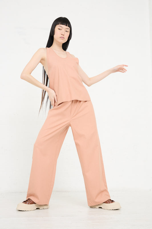 Woman in a sustainable fashion Baserange Wild Silk Apron Top in Sid Pink and wide-leg trousers posing against a white background.