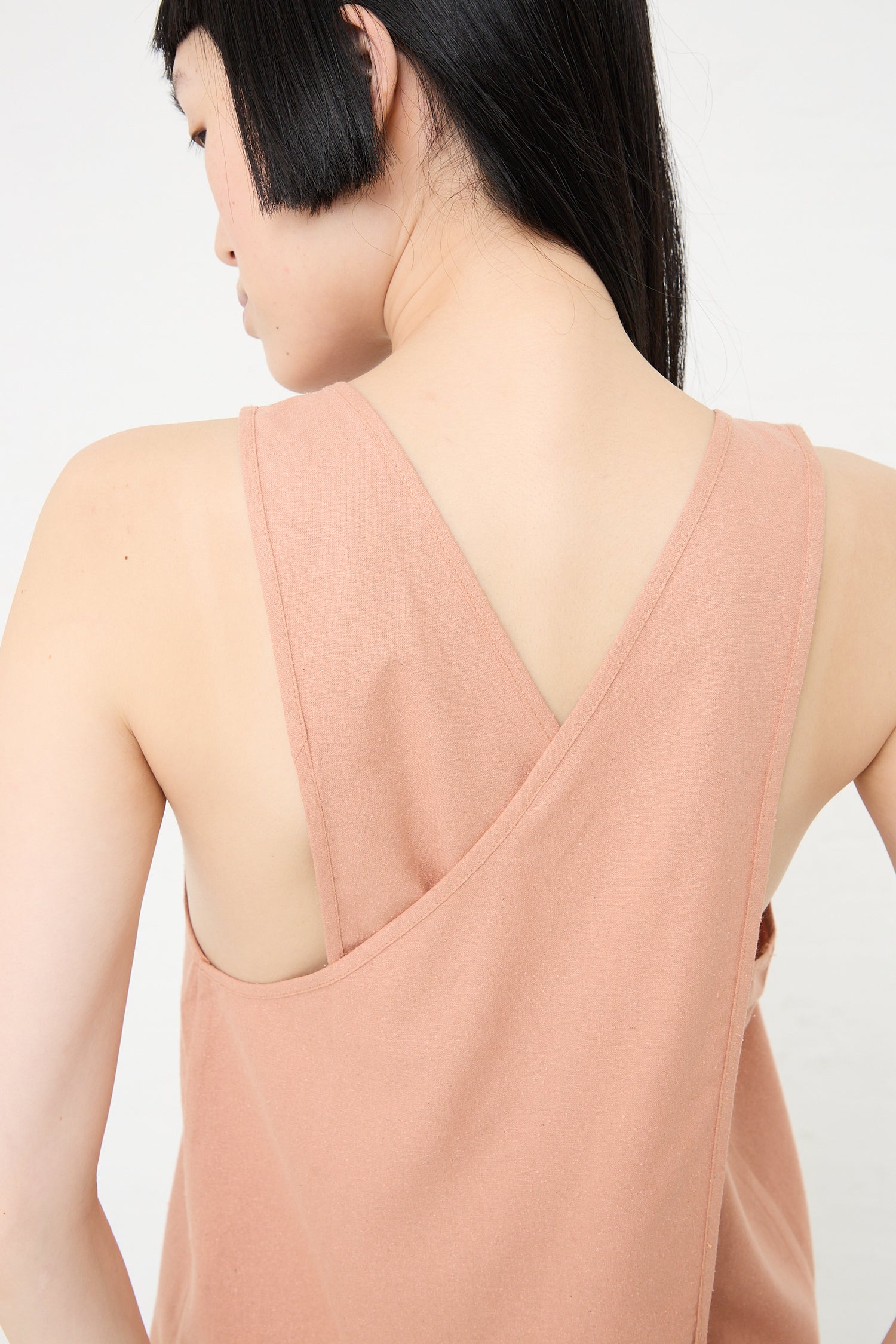 A woman with short hair wearing a sleeveless Wild Silk Apron Top in Sid Pink by Baserange with a v-back design, embodying sustainable fashion.