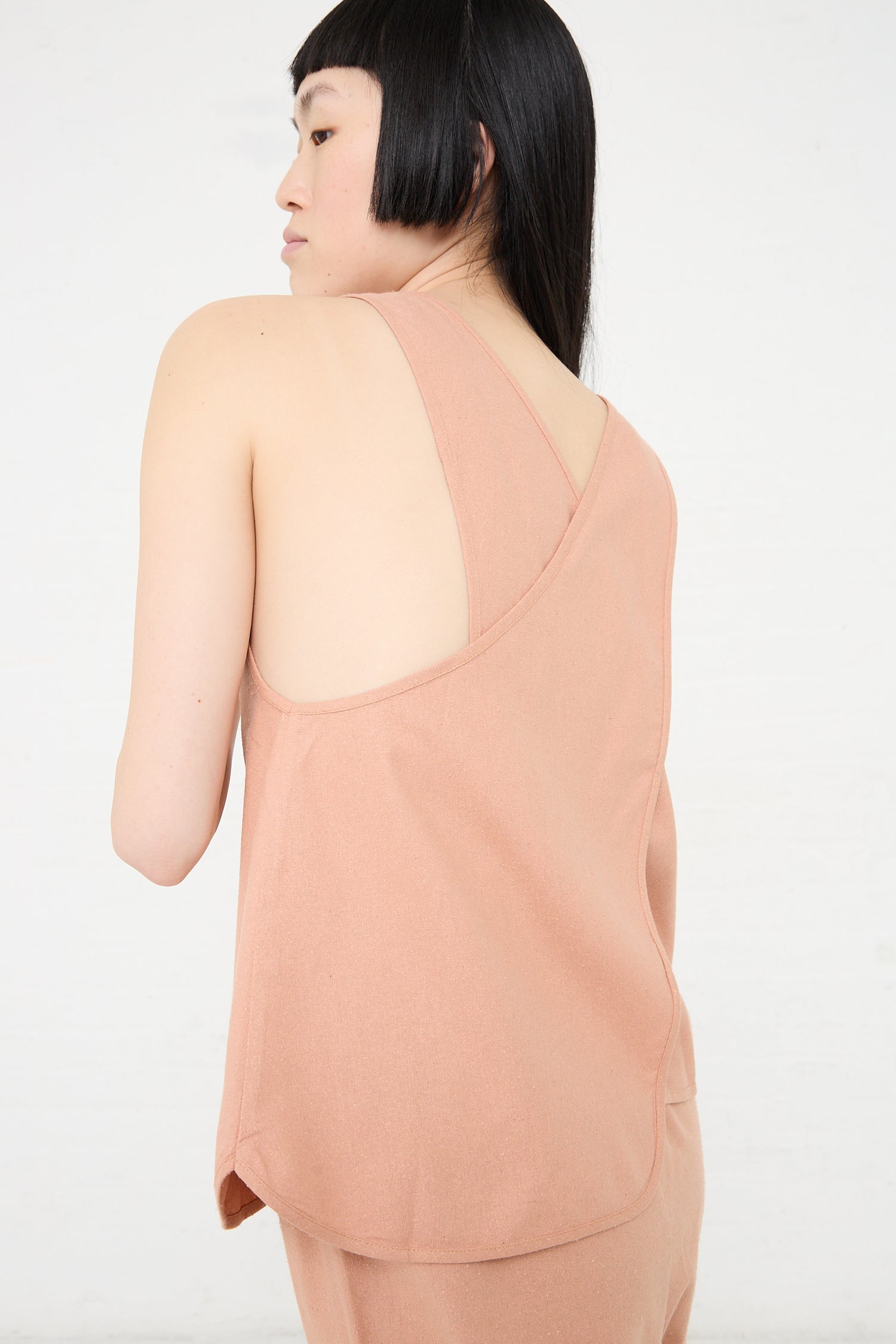 Woman wearing a sleeveless Wild Silk Apron Top in Sid Pink by Baserange, viewed from the back.
