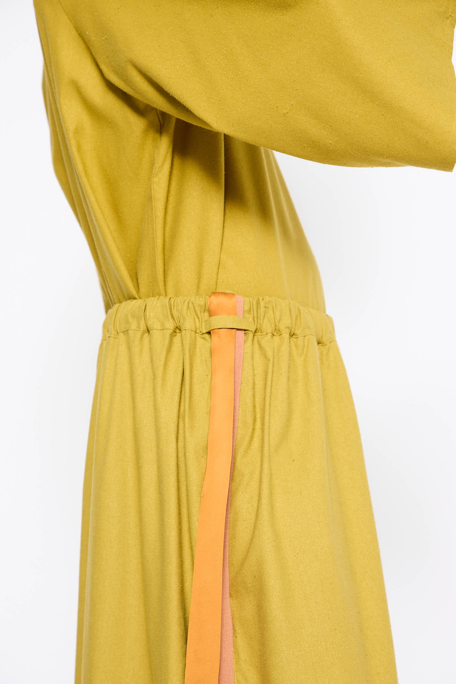 Close-up side view of the Wild Silk Cena Skirt in Sophos Green by Baserange, featuring a gathered waist detailing and an elasticated waistband, with an orange and pink stripe running down the side.