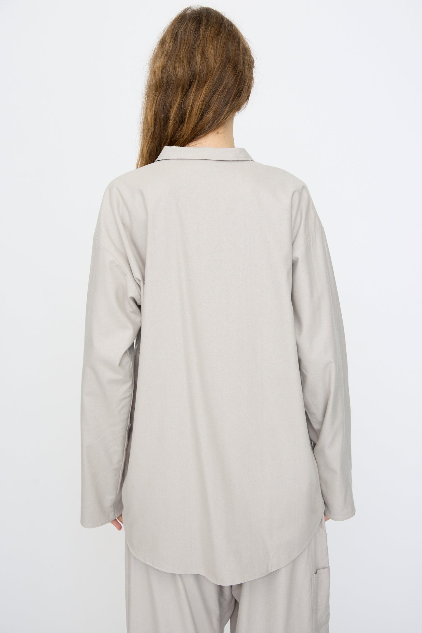 Person with long brown hair wears the Baserange Wild Silk Gren Overshirt in Prun Grey, shown from the back against a plain white background. The overshirt is made in Türkiye.