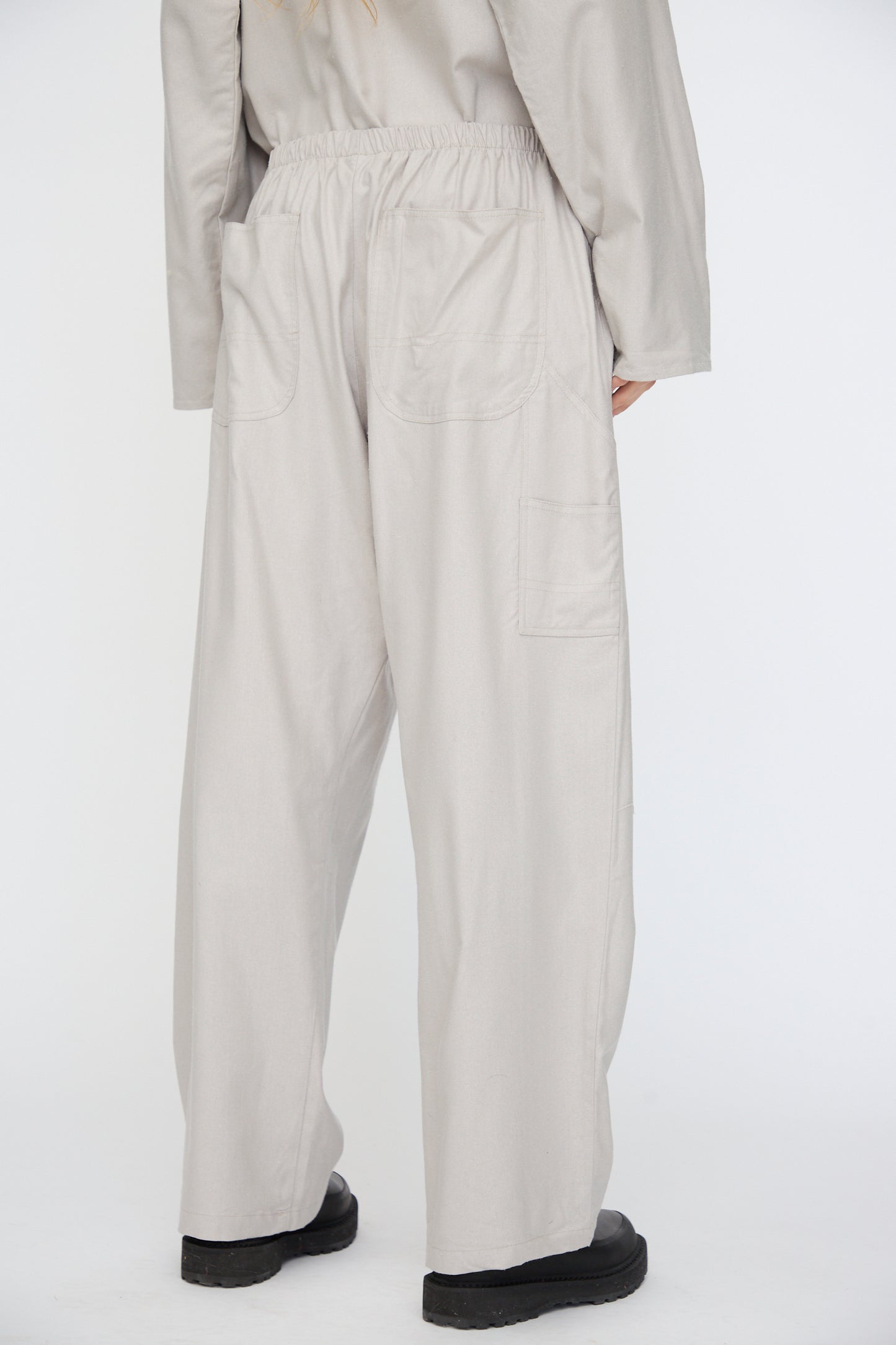 Person wearing Baserange Wild Silk Gren Pant in Prun Grey, featuring a relaxed fit, patch back pockets, and elastic waistband, viewed from behind against a plain white background.