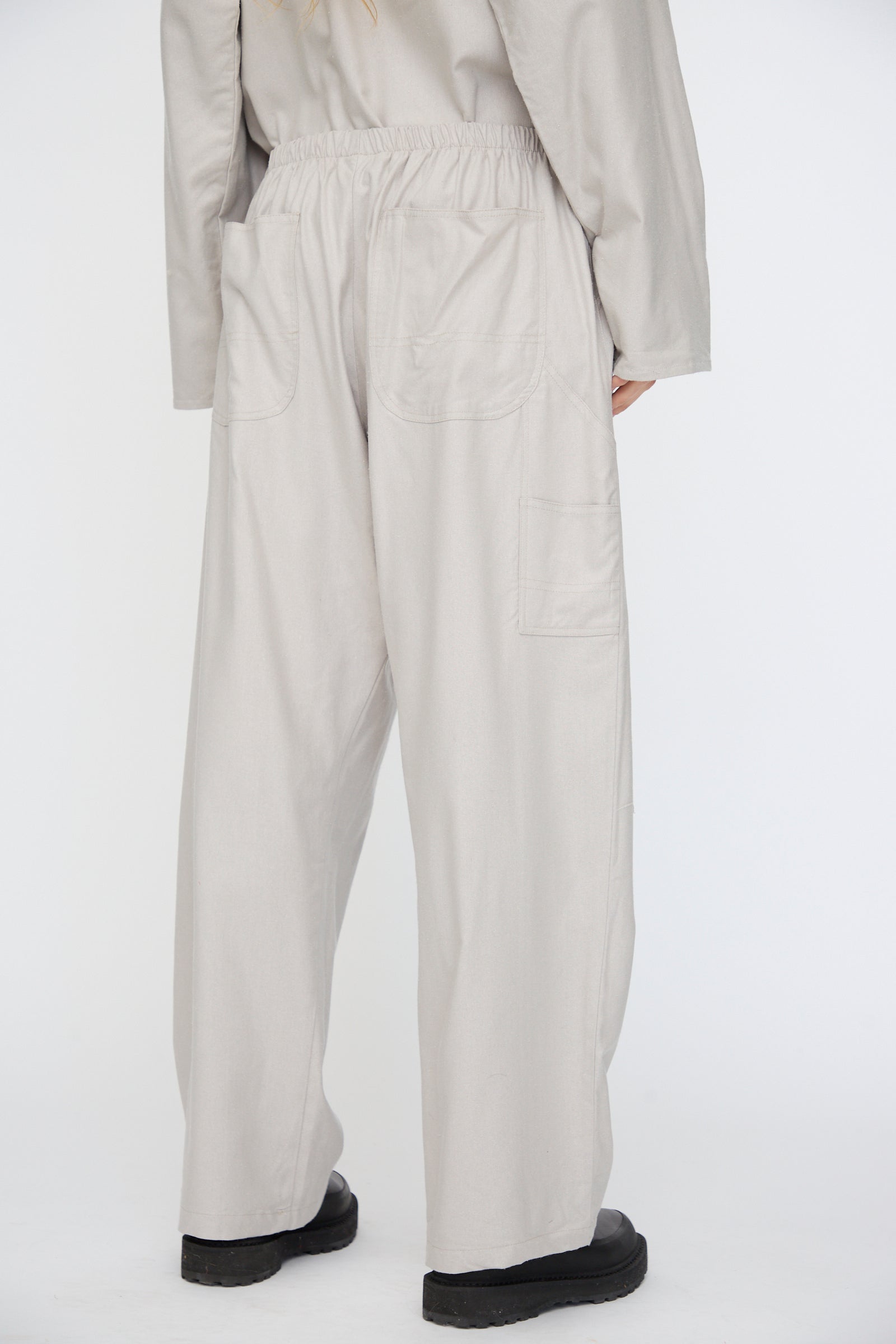 Person wearing Baserange Wild Silk Gren Pant in Prun Grey, featuring a relaxed fit, patch back pockets, and elastic waistband, viewed from behind against a plain white background.