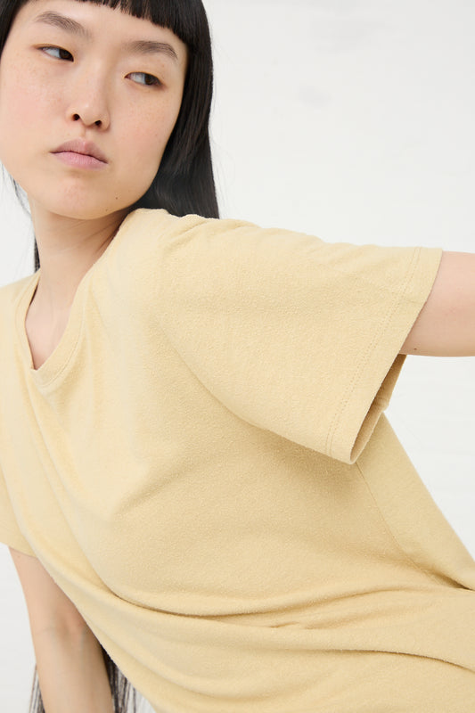 Close-up of a woman in a Baserange Wild Silk Jersey Tee in Oak Yellow looking away from the camera.