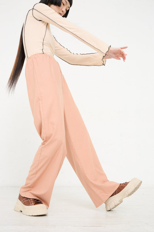 Woman in pastel outfit with Wild Silk Stoa Pant in Sid Pink by Baserange taking a step forward with an extended arm.