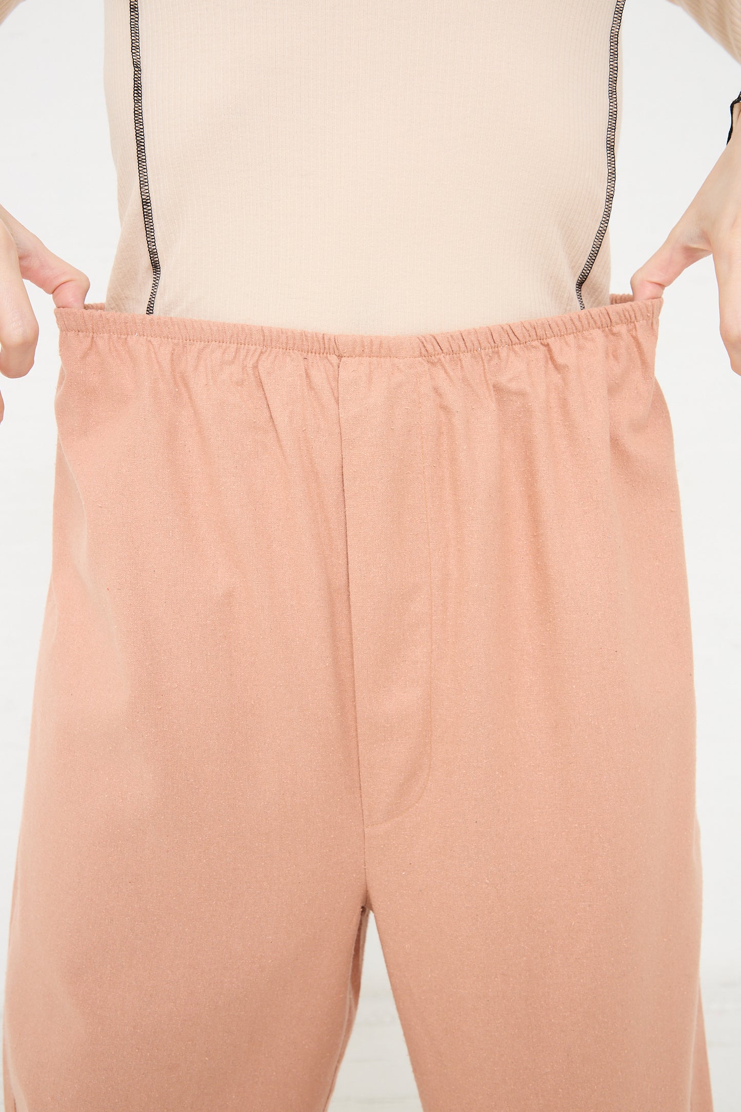 Person holding out the elastic waistband of their peach-colored Baserange Wild Silk Stoa Pant in Sid Pink to show relaxed fit.