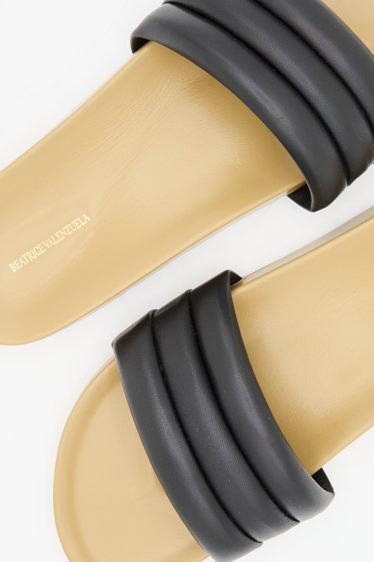The Classic Sandalia in Black by Beatrice Valenzuela features handcrafted beige slides with thick black lambskin uppers and the brand name printed on the footbed.