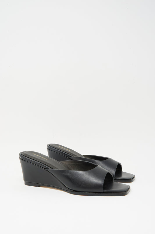 The Moderna Wedge Sandal in Black by Beatrice Valenzuela is a pair of open-toe black wedge-heeled mules made from supple Nappa cow leather, shown on a plain white background.