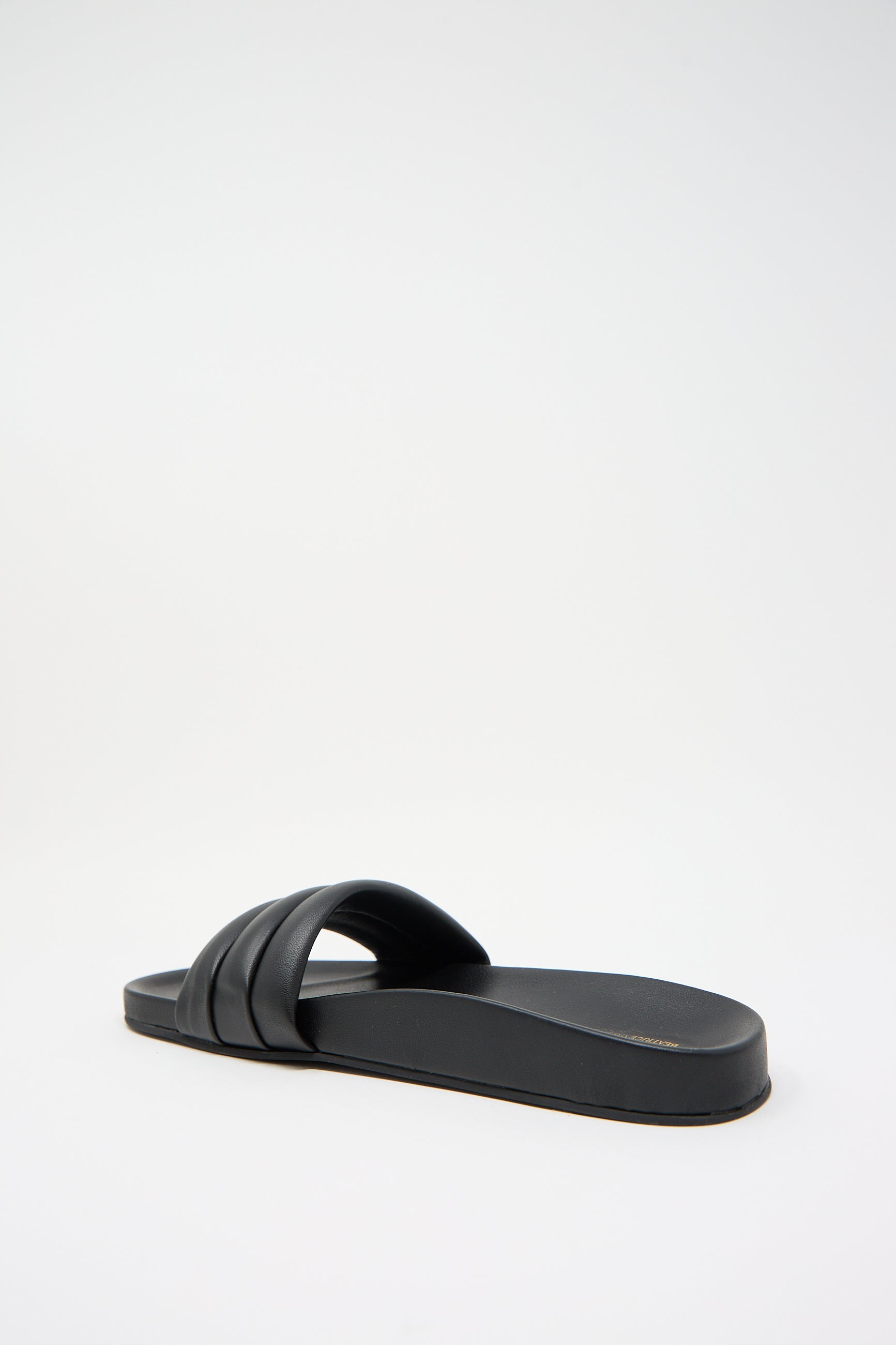 A handcrafted black sandal with a single wide lambskin strap and a flat sole, displayed against a plain white background. The Monocolor Sandalia in Black by Beatrice Valenzuela.