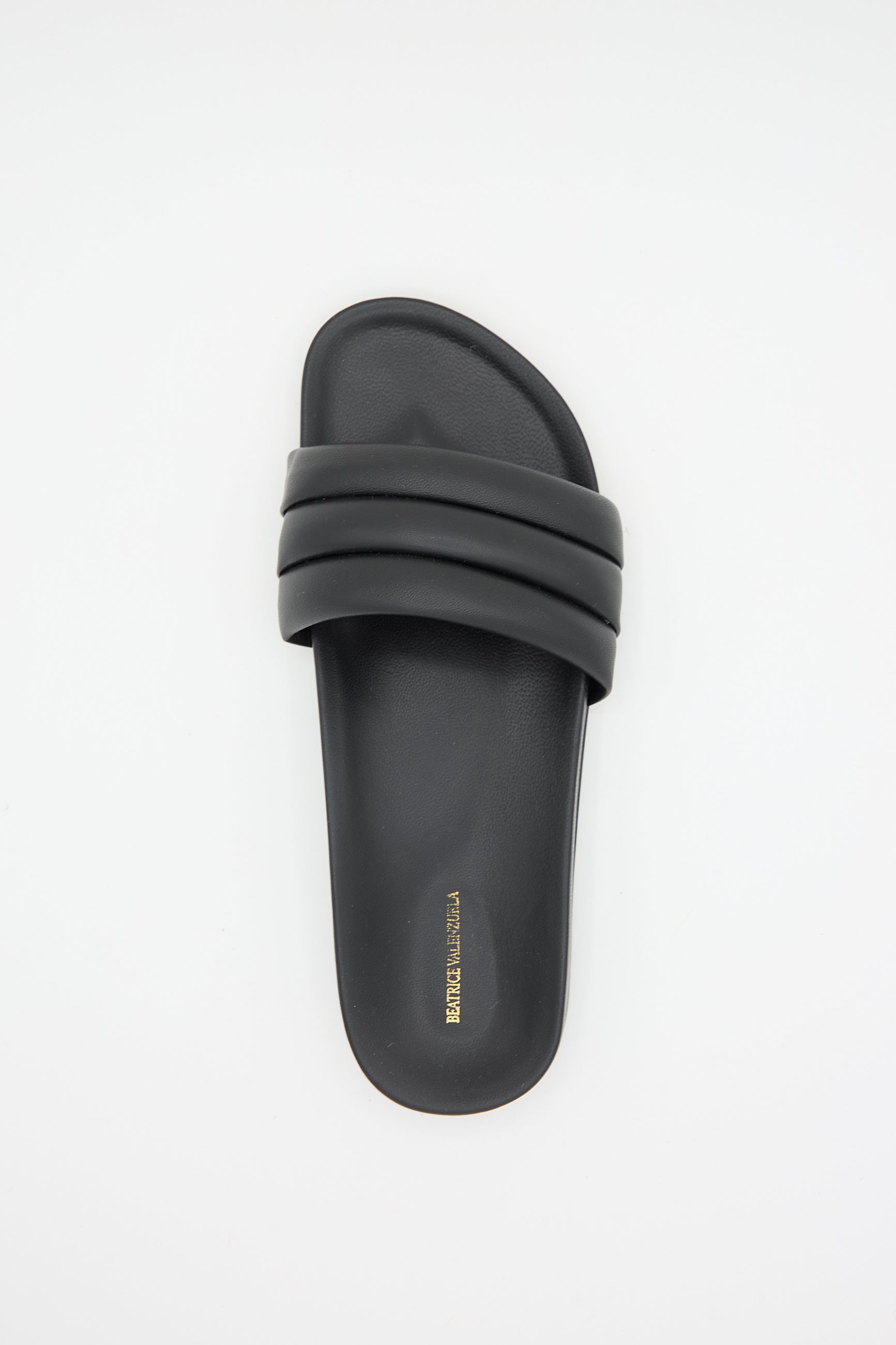 A single Monocolor Sandalia in Black with three padded straps across the top, featuring luxurious lambskin leather uppers and gold text branding on the insole by Beatrice Valenzuela.