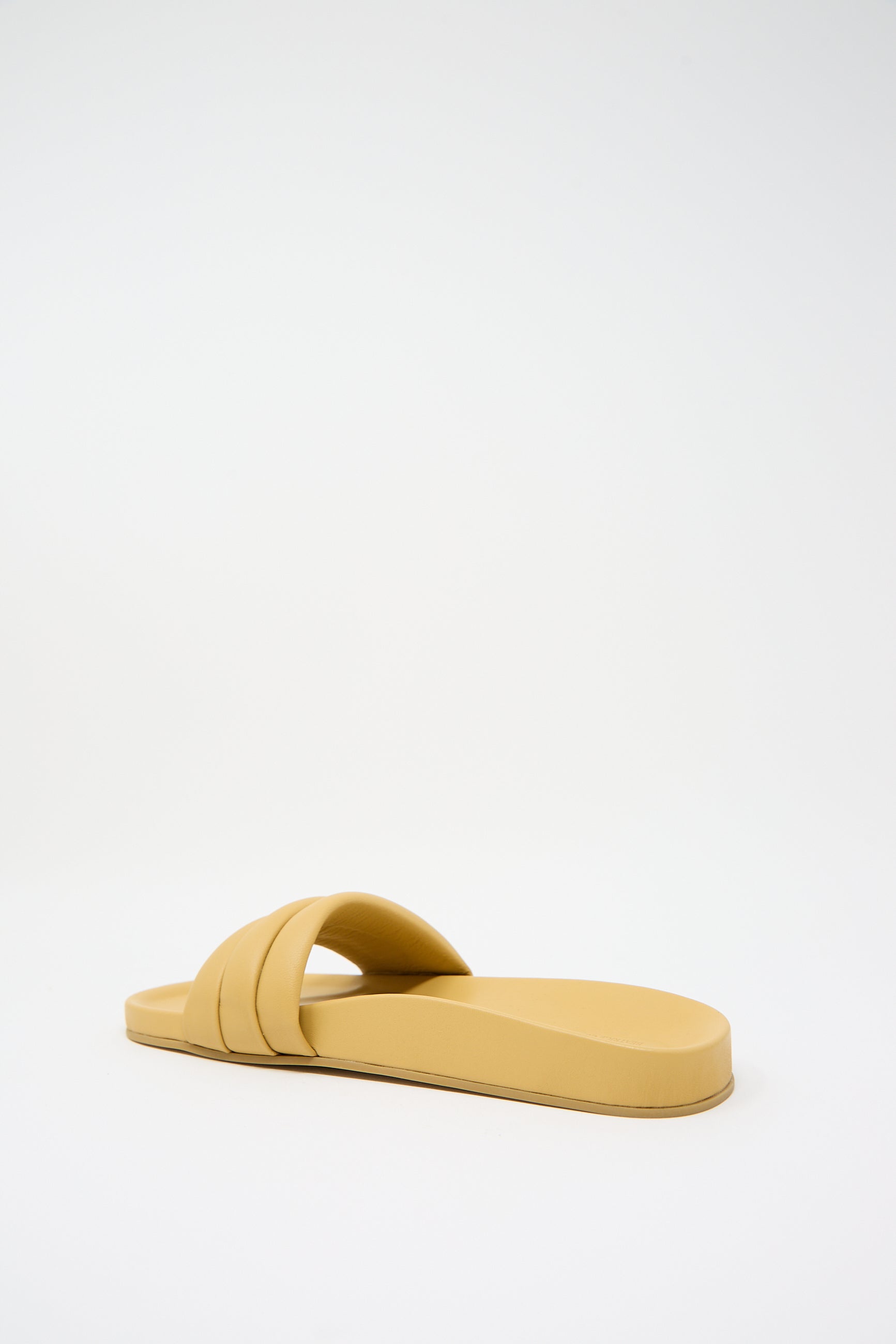 A single, beige-colored slip-on sandal with a double strap design made from luxurious lambskin uppers rests on a plain white background. It is the Monocolor Sandalia in Wheat by Beatrice Valenzuela.