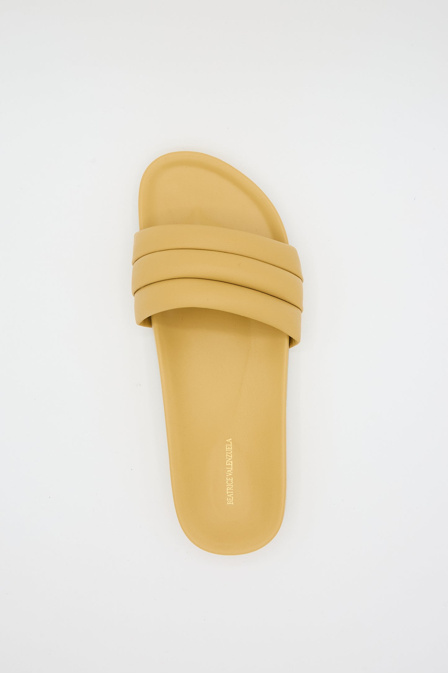 A single Monocolor Sandalia in Wheat by Beatrice Valenzuela with a wide lambskin upper strap and slightly contoured footbed, handcrafted from 100% leather, against a plain white background.