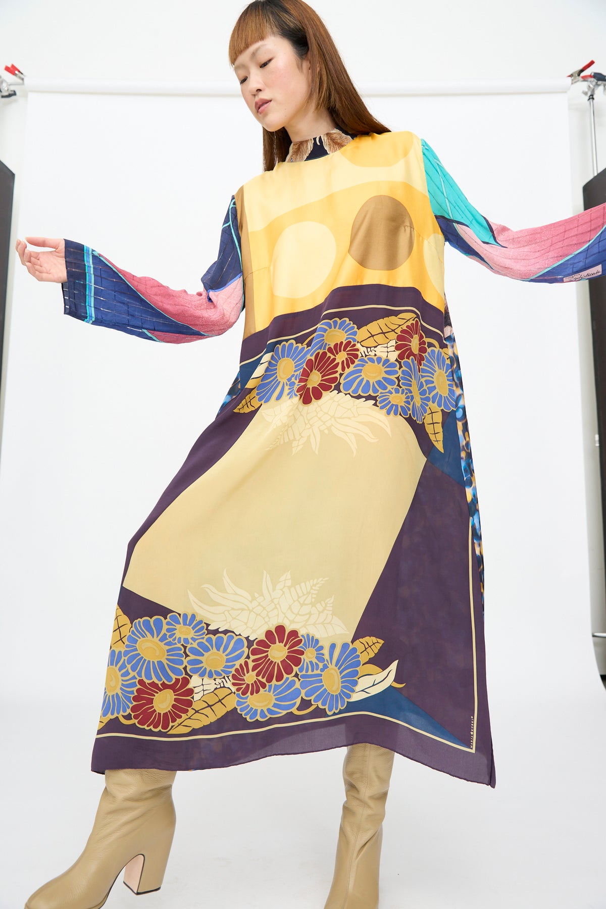 Model wearing a Bettina Bakdal Classic Mandarin Collar Dress in Alice Vollmer, a long-sleeved, knee-length up-cycled silk dress with a multi-colored abstract floral print, styled with tan boots.