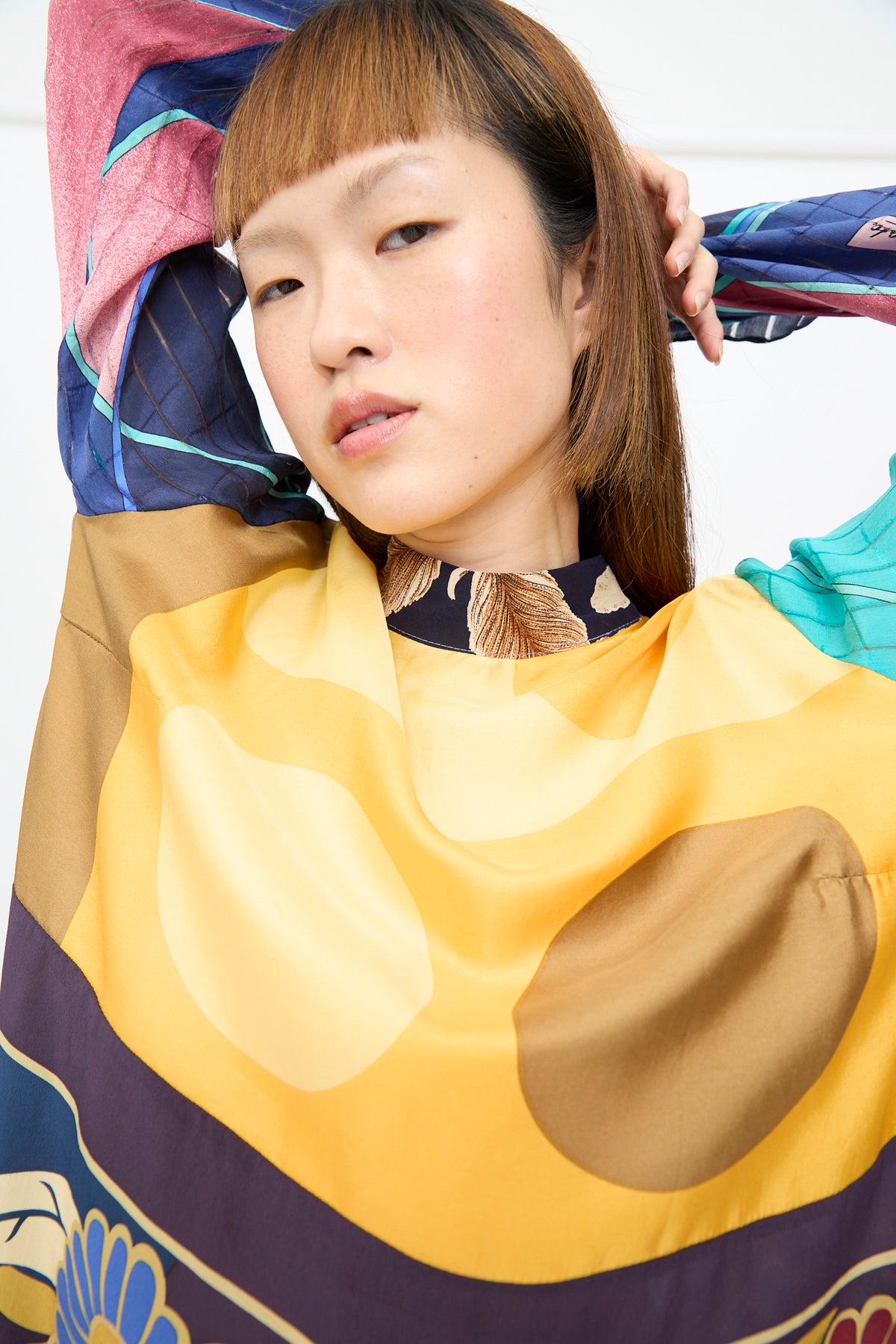 A person wears a Bettina Bakdal Classic Mandarin Collar Dress in Alice Vollmer, an up-cycled silk dress with long sleeves and a vibrant, multicolored abstract geometric print.