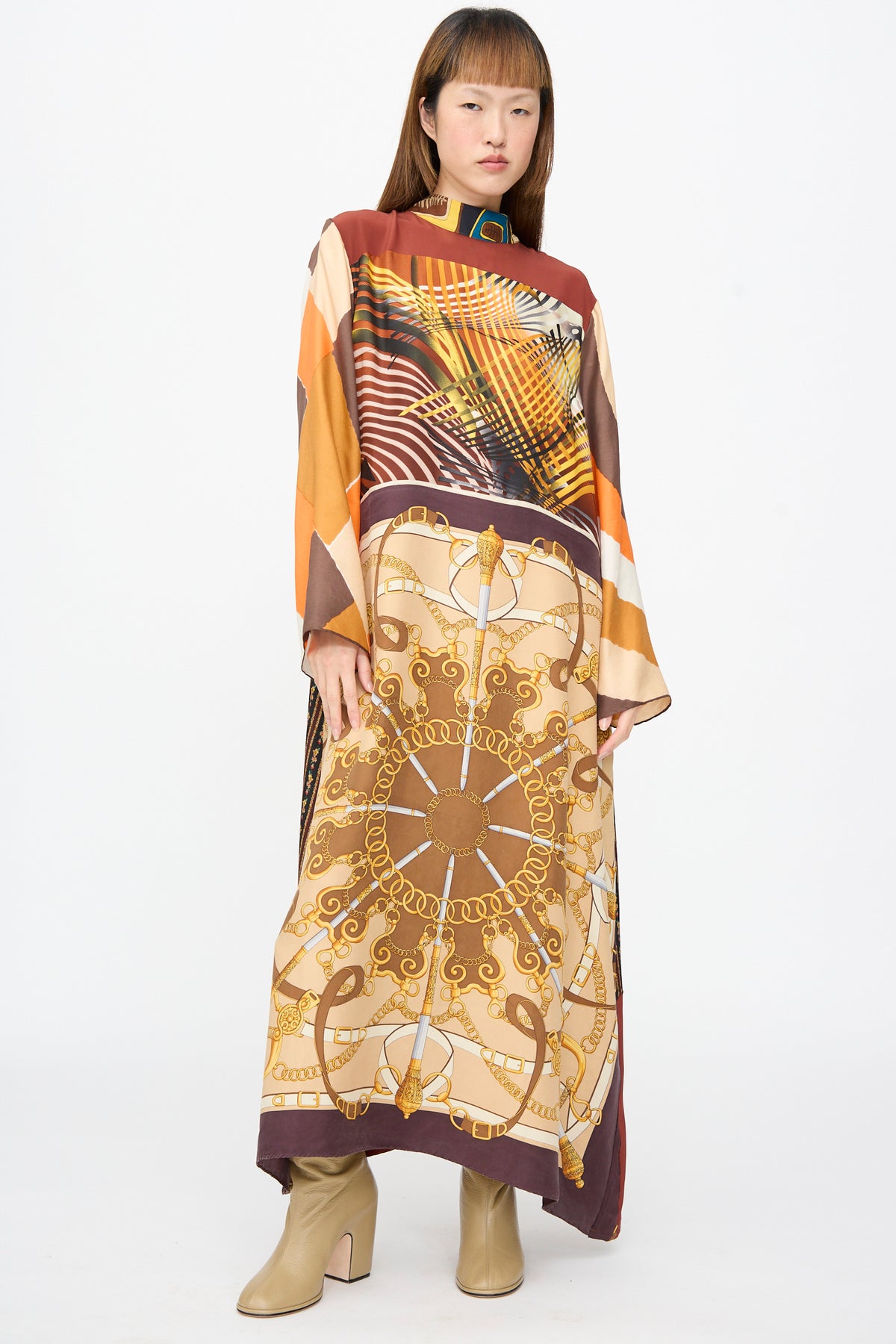 A person wears a Bettina Bakdal Classic Mandarin Collar Dress in Benita Otte, an up-cycled silk dress with a colorful abstract and chain-link pattern, paired with beige block-heeled boots.