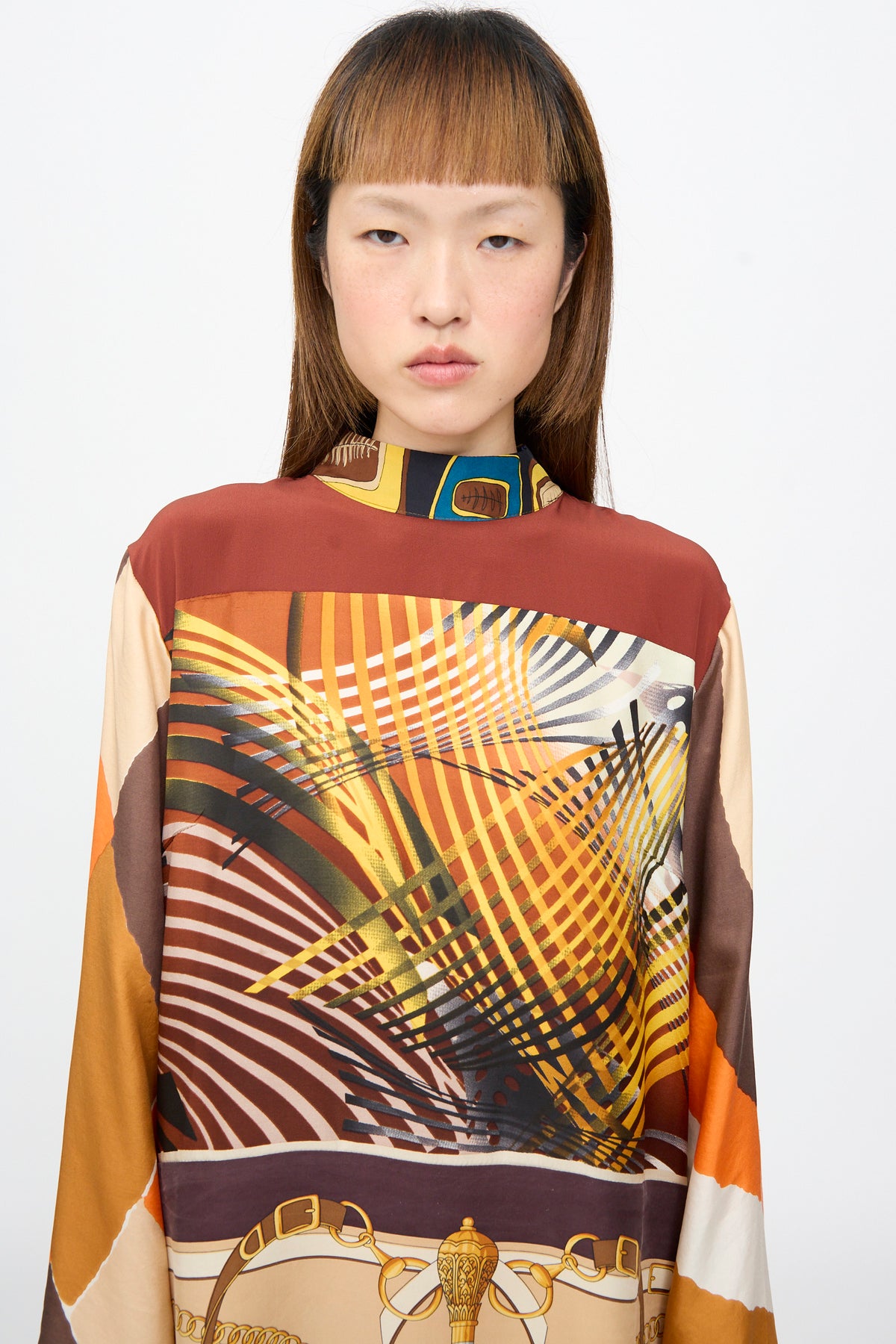 Bettina Bakdal Classic Mandarin Collar Dress in Benita Otte, featuring a long-sleeve, mandarin collar silhouette with brown, orange, and yellow geometric lines and a gold-toned chain pattern at the hem.