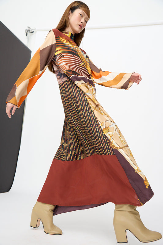 A person wearing a Bettina Bakdal Classic Mandarin Collar Dress in Benita Otte, featuring a long-sleeved up-cycled silk midi silhouette with a colorful geometric and chain-link pattern and tan block-heeled boots.
