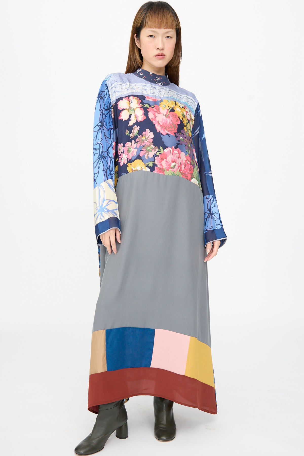 A model wears the Bettina Bakdal Classic Mandarin Collar Dress in Grete Willers, an up-cycled silk dress featuring a mandarin collar, blue and pink floral patterns, a grey midsection, and geometric hem.