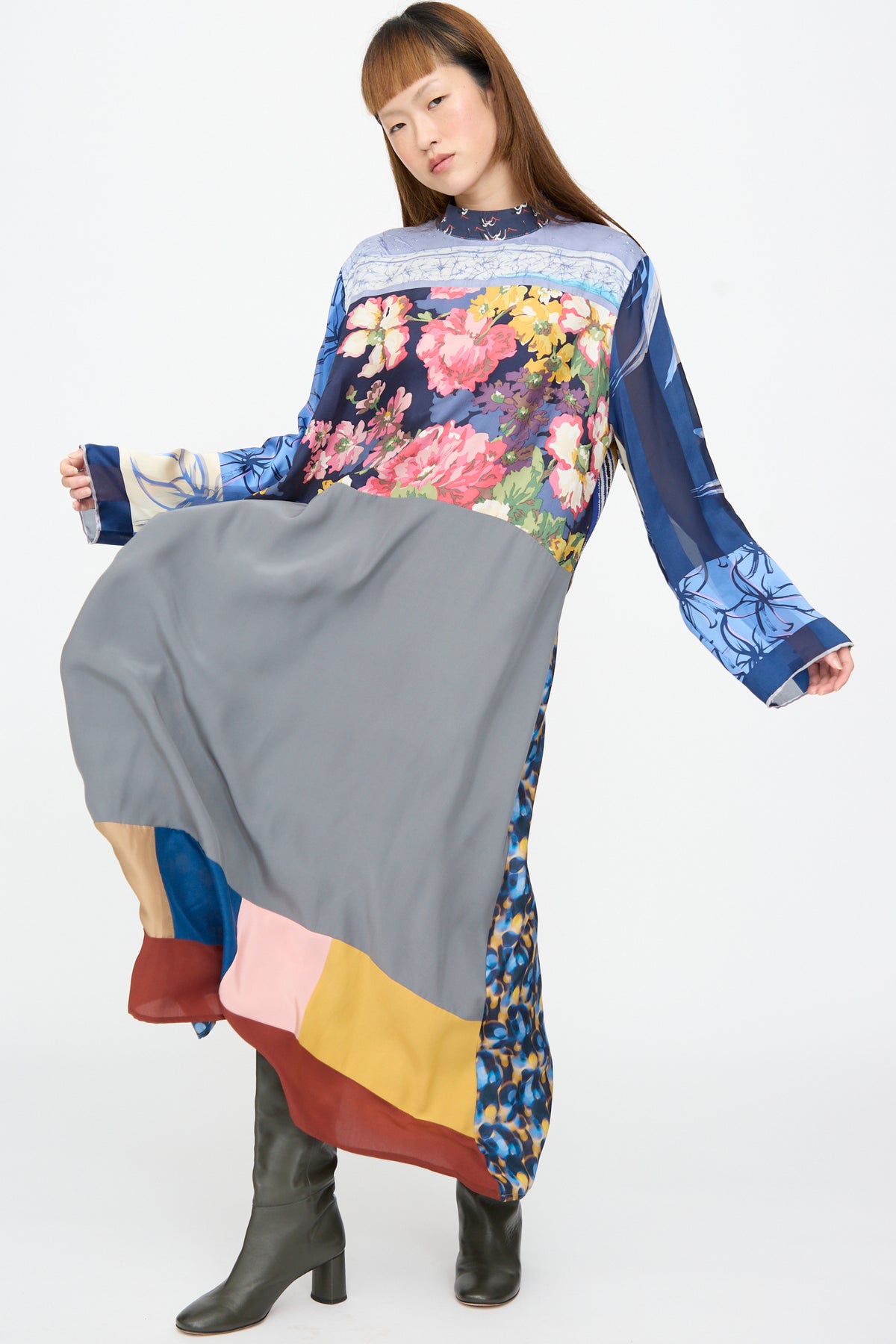 A person wears a Bettina Bakdal Classic Mandarin Collar Dress in Grete Willers, a long-sleeved, knee-length up-cycled silk dress with a patchwork of floral prints and solid panels, paired with dark boots.