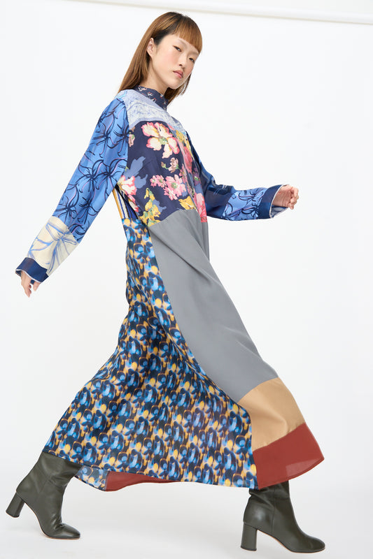 A person wears a Bettina Bakdal Classic Mandarin Collar Dress in Grete Willers, an up-cycled long-sleeved silk dress with a patchwork of floral and abstract blue, grey, and brown patterns, and olive boots.