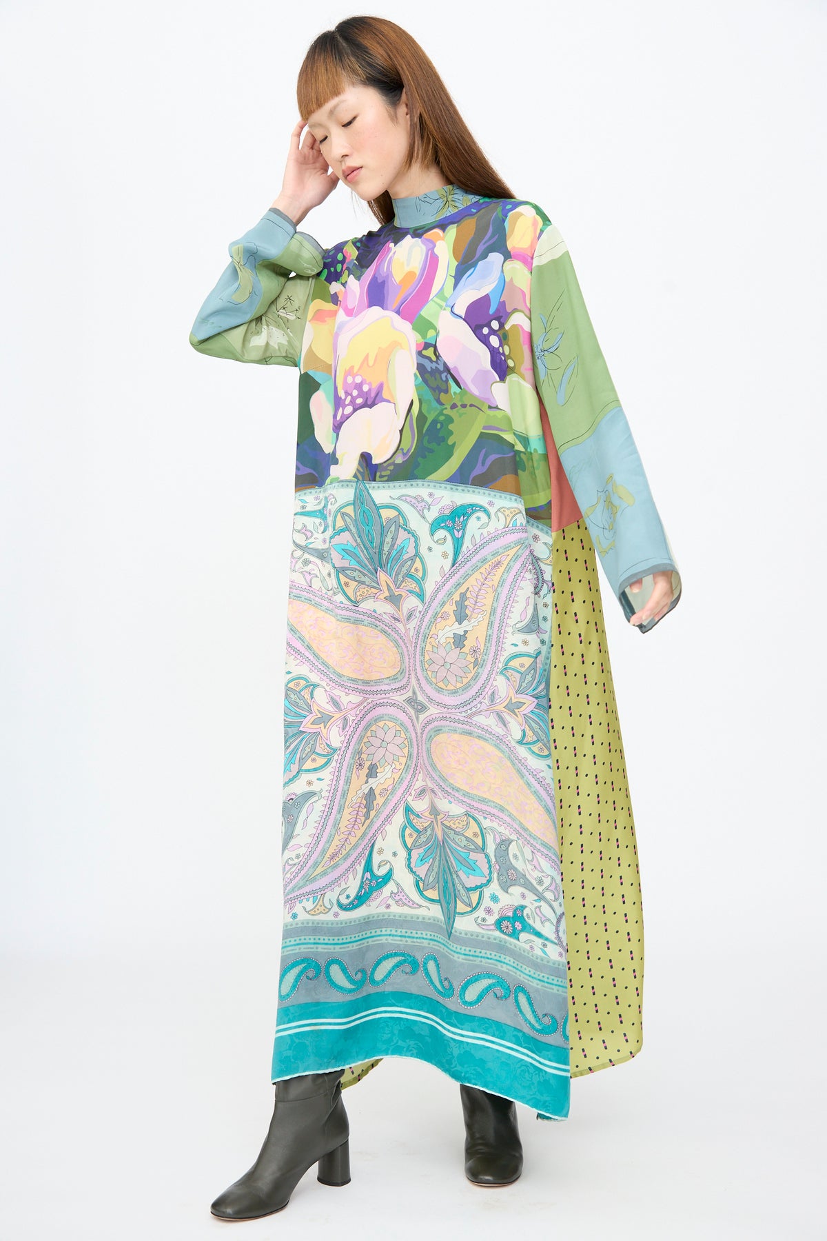 A person wears a Bettina Bakdal Classic Mandarin Collar Dress in Hedwig Arheim, a vintage silk, ankle-length dress featuring a mix of floral, paisley, and polka dot patterns, styled with dark heeled boots.