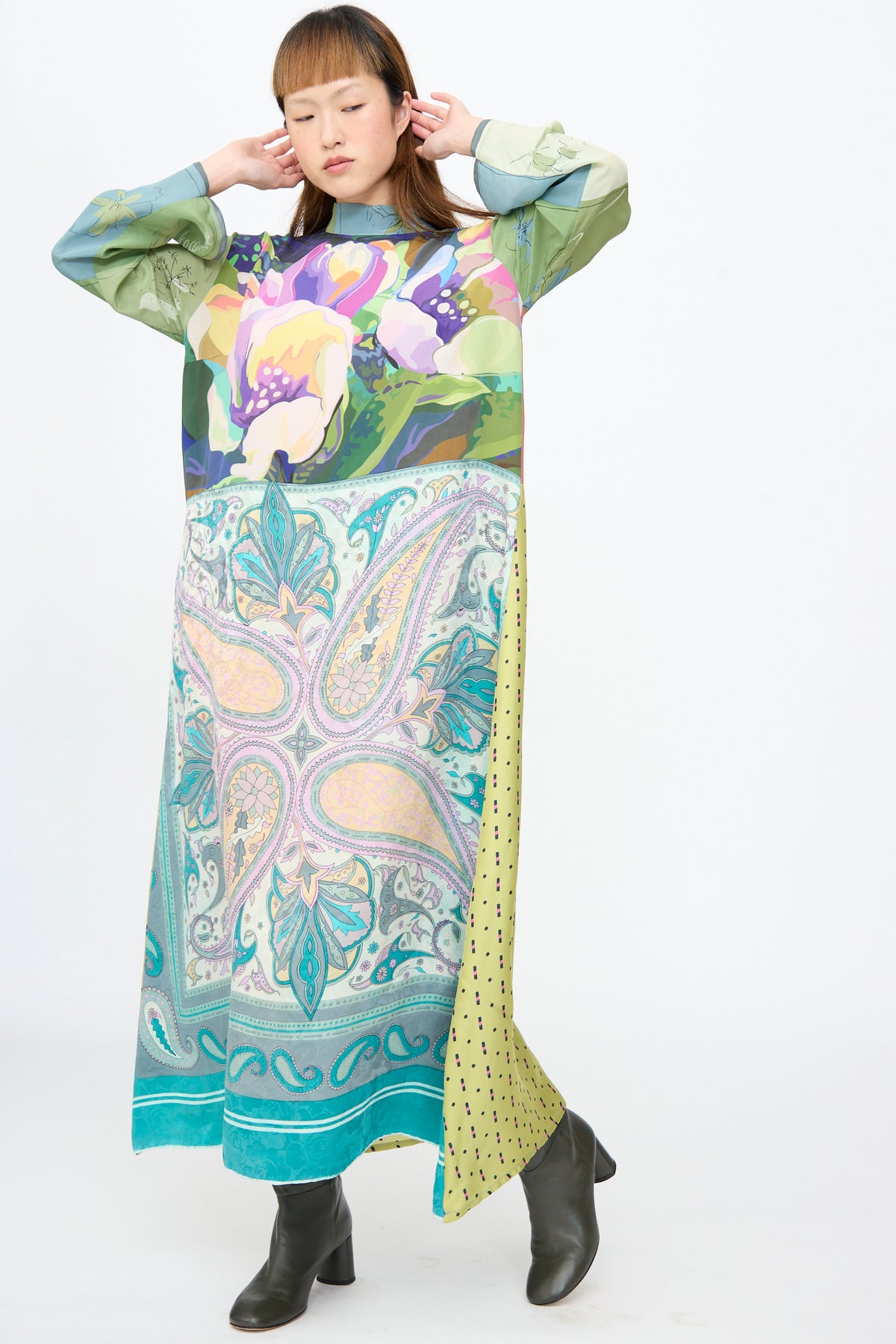 A person wears a Bettina Bakdal Classic Mandarin Collar Dress in Hedwig Arheim, an up-cycled silk dress with long sleeves, ankle-length hem, a floral top, paisley bottom, and dark ankle boots.