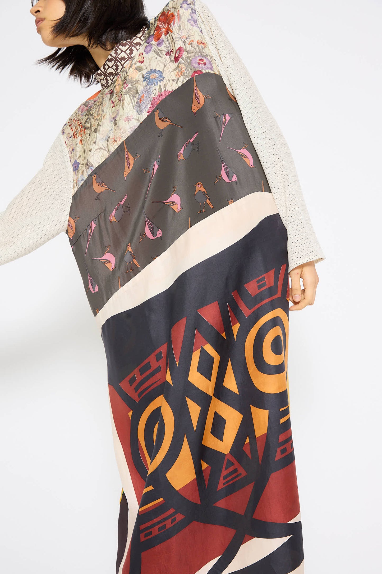 A person wearing the Classic Mandarin Collar Dress in Little Pink Songbird by Bettina Bakdal, crafted from up-cycled vintage silk scarves with floral, bird, and geometric patterns, stands against a plain background.
