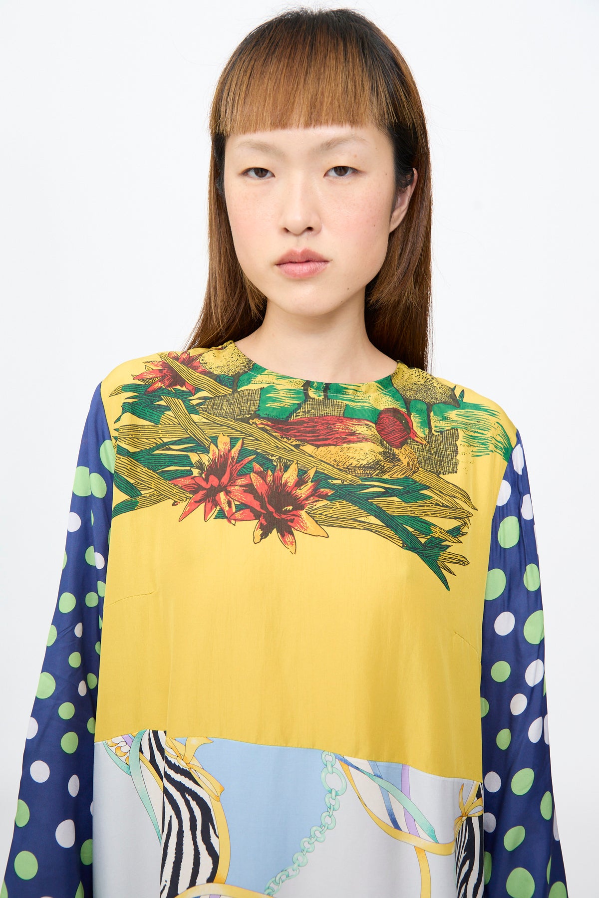 The Hannah Dress in Friederike Dicker is an up-cycled silk dress featuring a yellow bird-and-floral bodice, blue polka-dot sleeves, and a light blue hem with a zebra-stripe and chain motif.