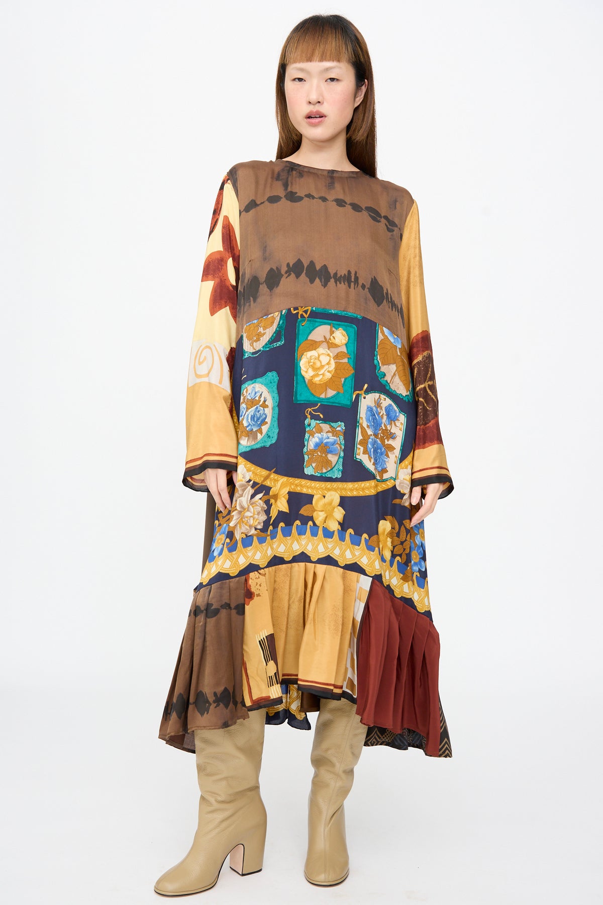 A person wears the Bettina Bakdal Hannah Dress in Ise Gropius, a long-sleeved vintage silk midi dress with patchwork floral, geometric, and abstract patterns in brown, blue, and gold, and tan boots.
