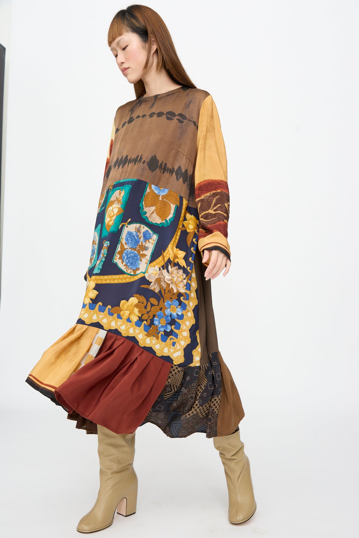A model wears the Bettina Bakdal Hannah Dress in Ise Gropius, a long-sleeved, knee-length up-cycled silk dress featuring brown, blue, and yellow floral and geometric patterns, paired with tan boots.