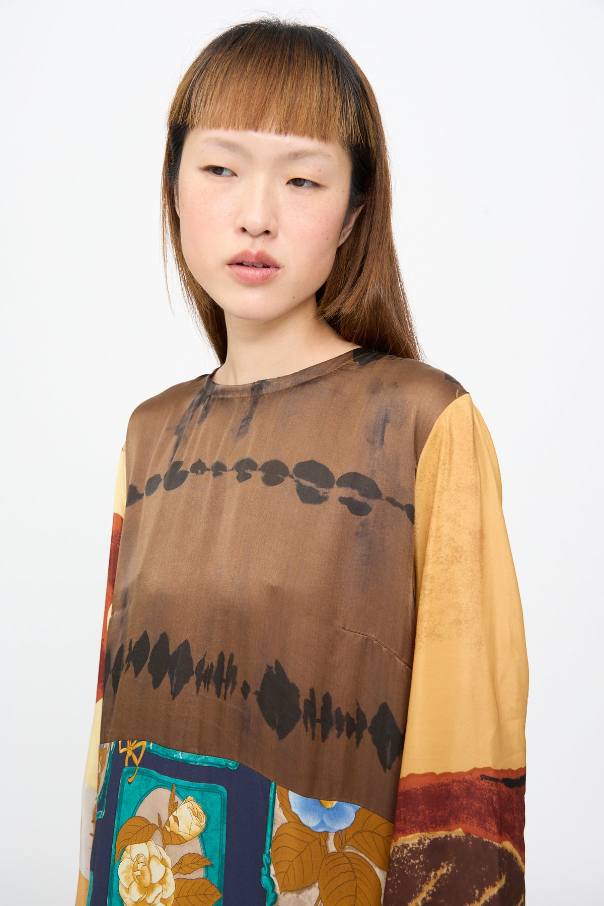A woman wearing the Bettina Bakdal Hannah Dress in Ise Gropius, a long-sleeved silk dress with a brown patterned bodice, yellow sleeves, and a colorful floral print along the hem.
