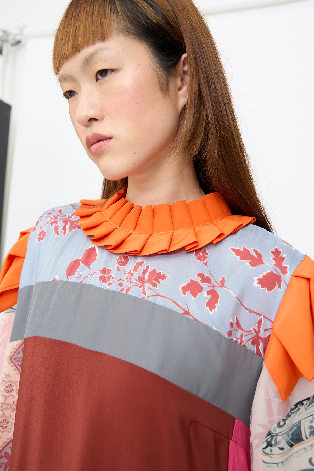 Bettina Bakdal Ruffled Collar and Shoulder Dress in Grit Kallin, an up-cycled silk dress featuring an orange ruffled collar and sleeves with a color-blocked design of grey, dark red, and blue floral fabric.