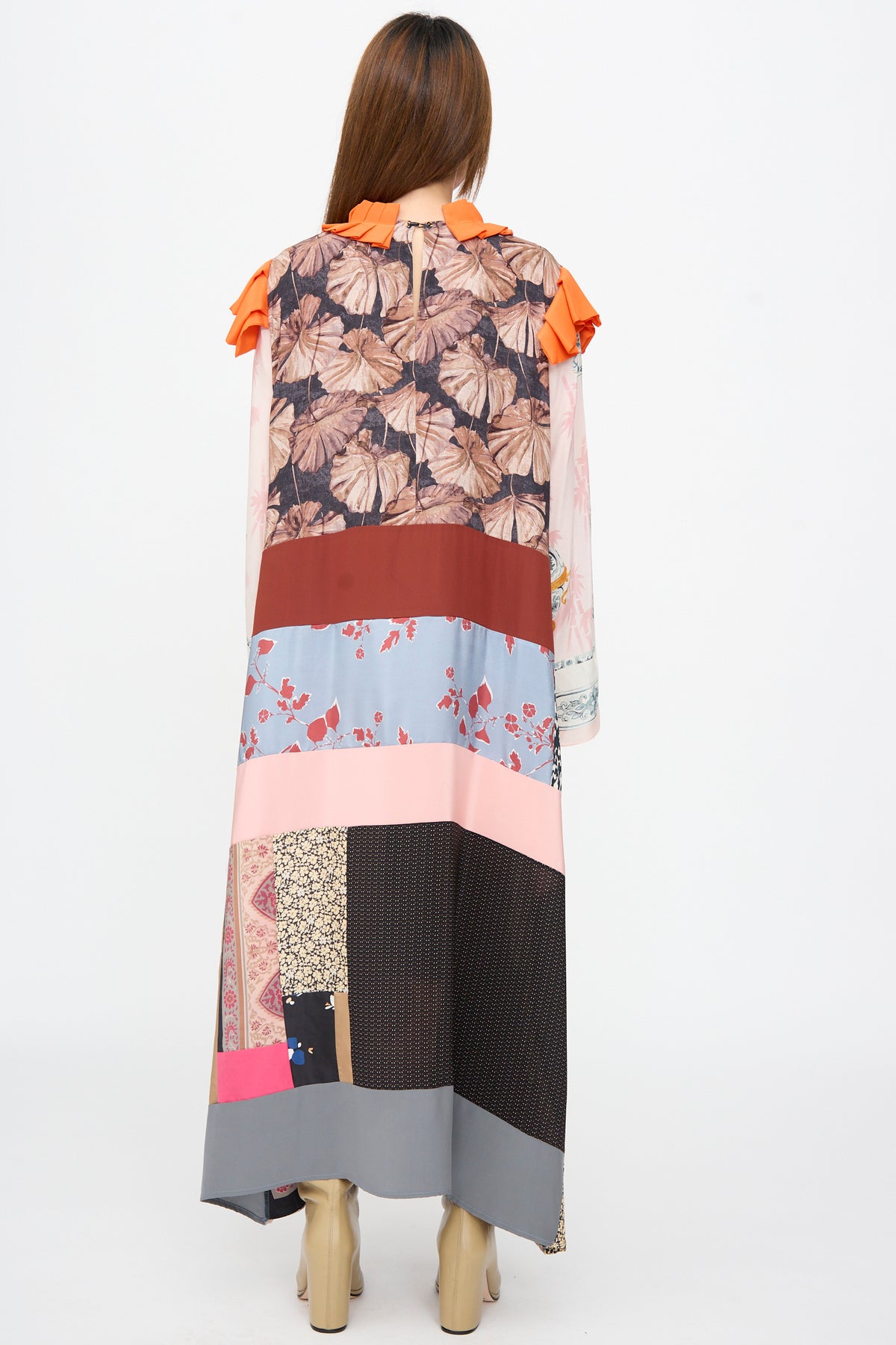 A woman seen from behind in the Bettina Bakdal Ruffled Collar and Shoulder Dress in Grit Kallin, featuring an up-cycled patchwork midi design with a bright orange ruffled collar and shoulder details.